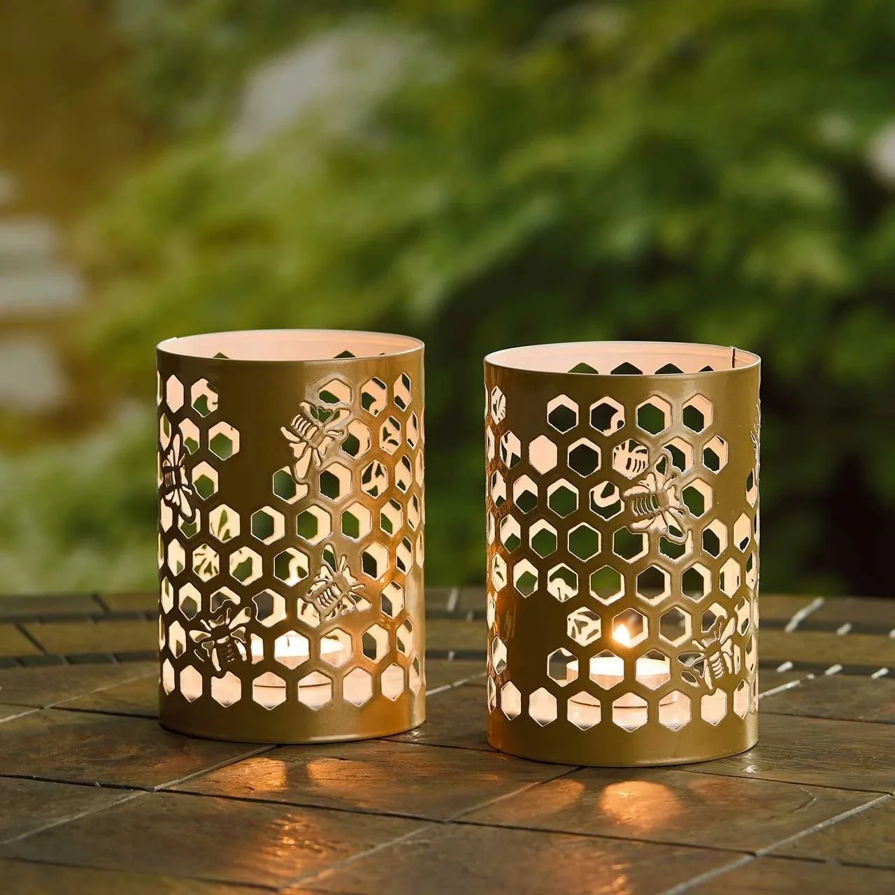 Two golden lanterns with tea lights in them, the holes in the lantern are shaped like honeycomb