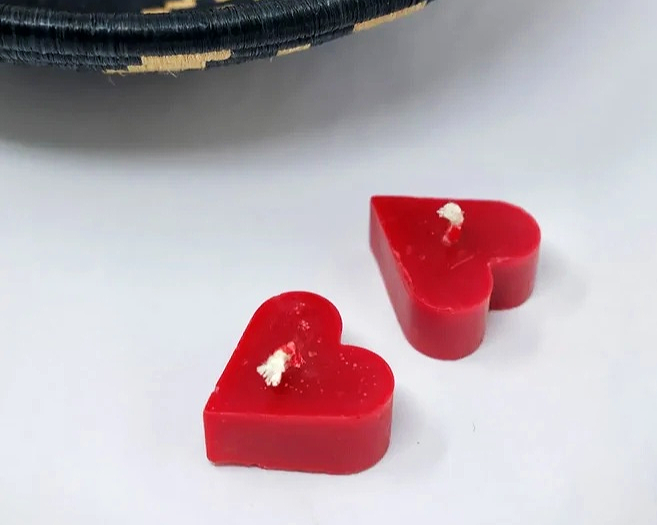 Two red heart-shaped candles on a white surface