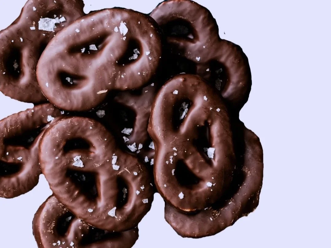 A pile of chocolate covered pretzels with sea salt on a light purple background