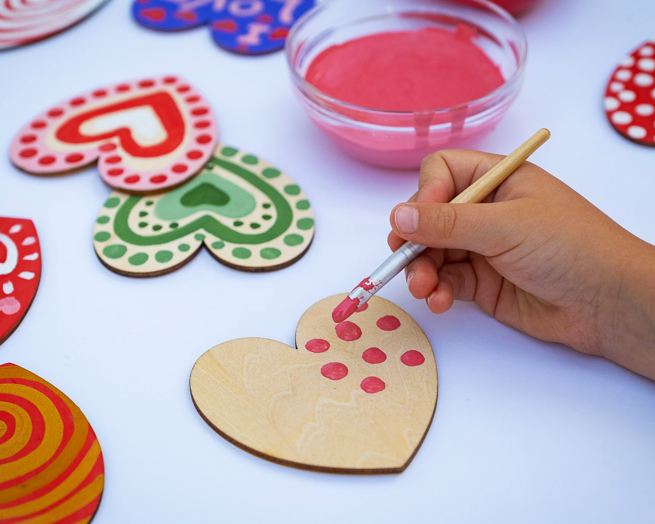 A scattering of wooden hearts with painted patterns - on the right is a hand painting one of the hearts