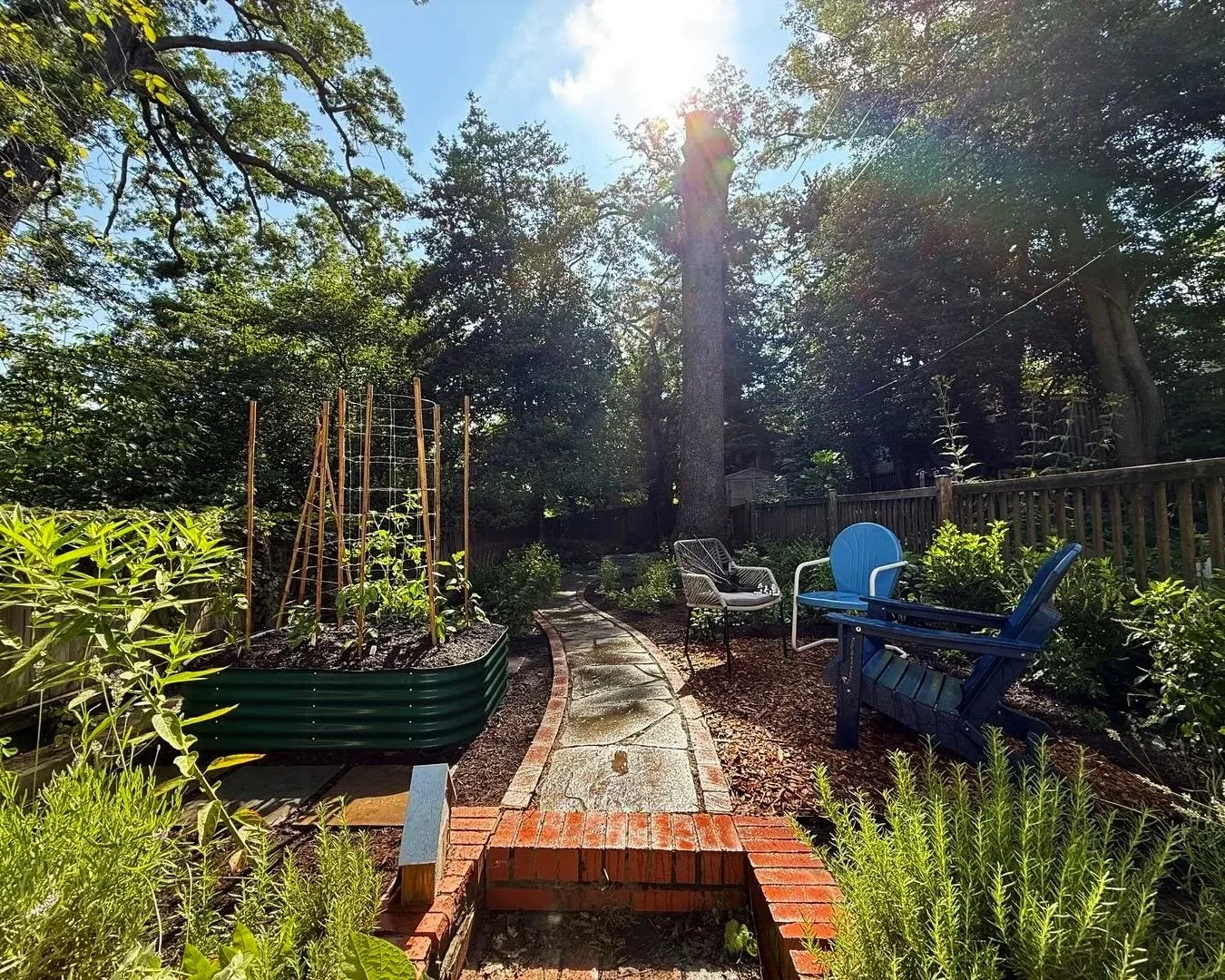 A shot of a garden featuring aidrondack chairs, a raised bed with planting trellises, and a stone path