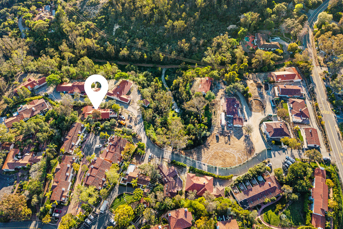 Aerial view of a neighborhood with houses, trees, and a street. A white location pin marker is over a specific property.