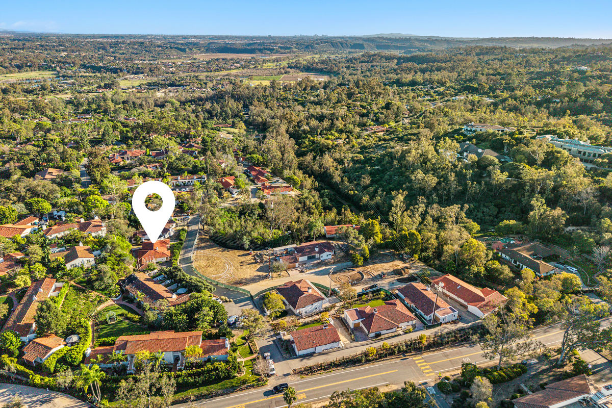 Aerial view of a neighborhood with houses, trees, and a park with a pin marker indicating a specific location.