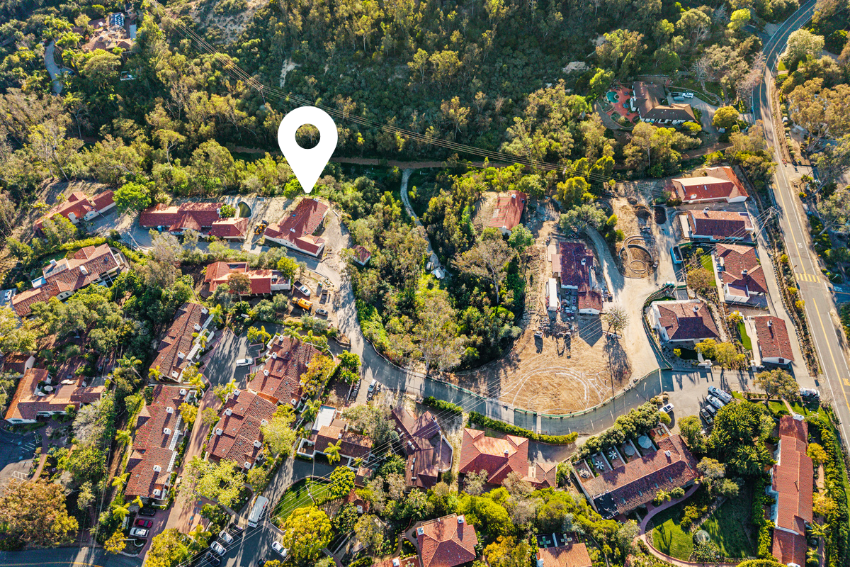 Aerial view of a neighborhood with houses, trees, and a basketball court, with a location marker pointing to a specific house.