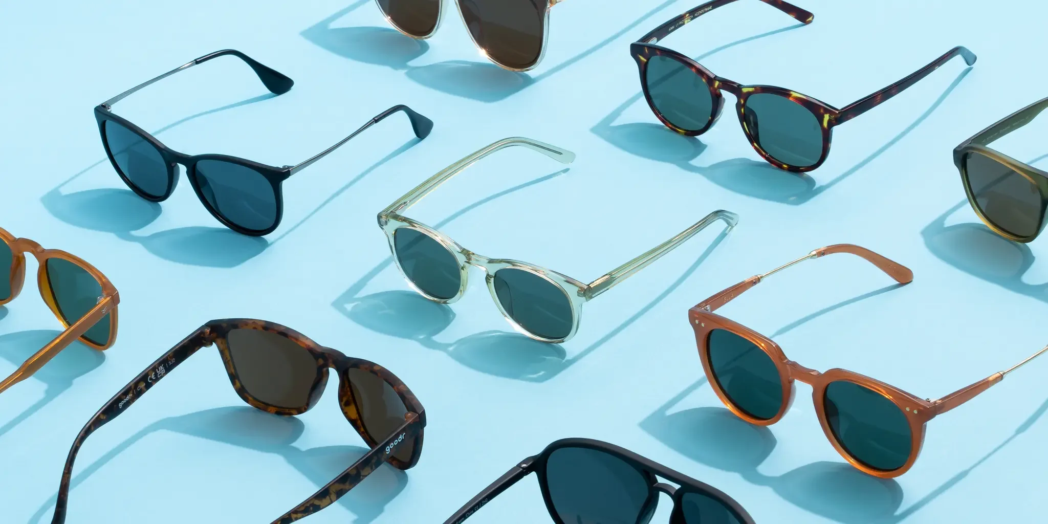 Collection of sunglasses with various frame designs and colors displayed on a light blue surface.