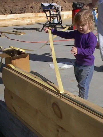 A little girl pulling waterproof sealing off a log for a home build.