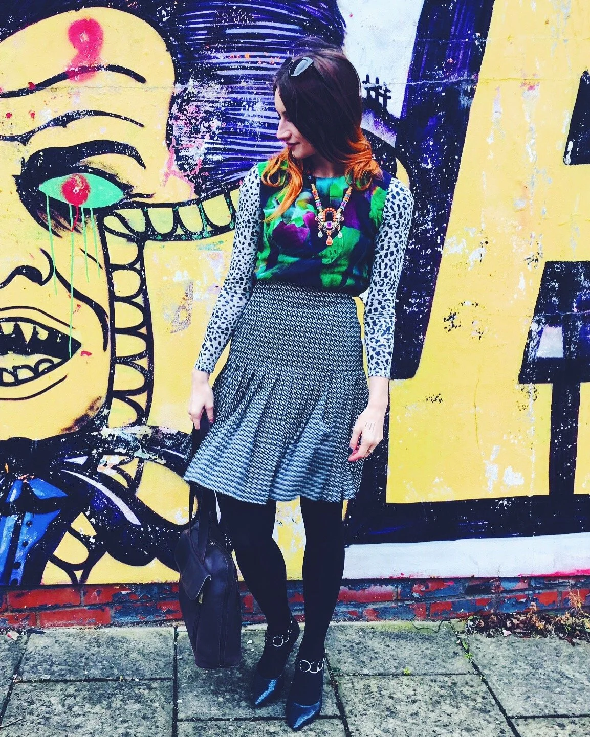 Louisa Rogers wearing a bold pattern-mixed outfit featuring animal print sleeves, a floral top, and geometric skirt, posing in front of a vibrant graffiti wall in Brighton street style photography.