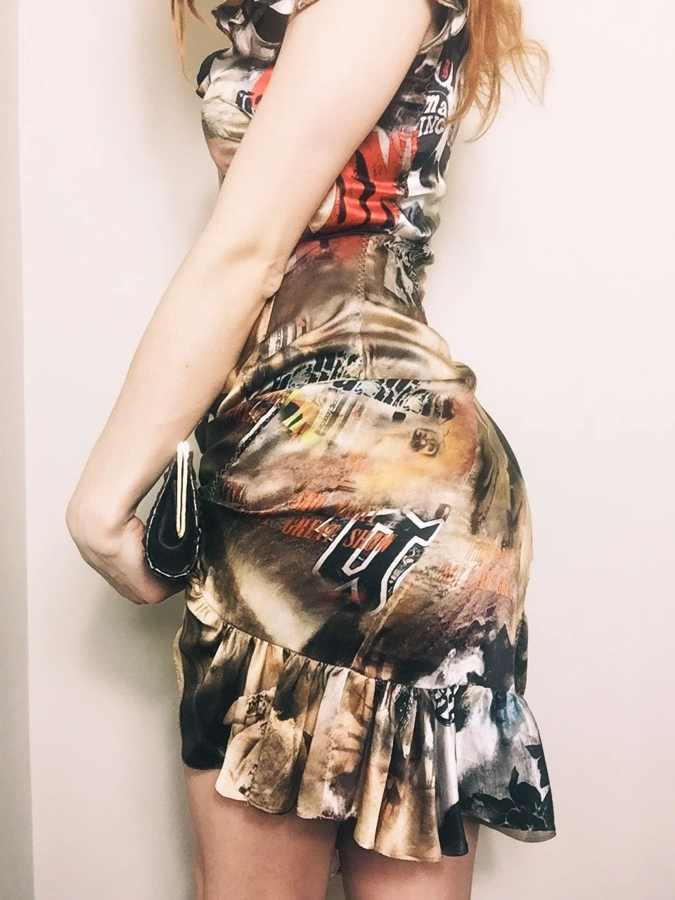 Side view of a woman wearing a fitted mini dress with ruffled hem and bold graphic print, styled with a black textured clutch.