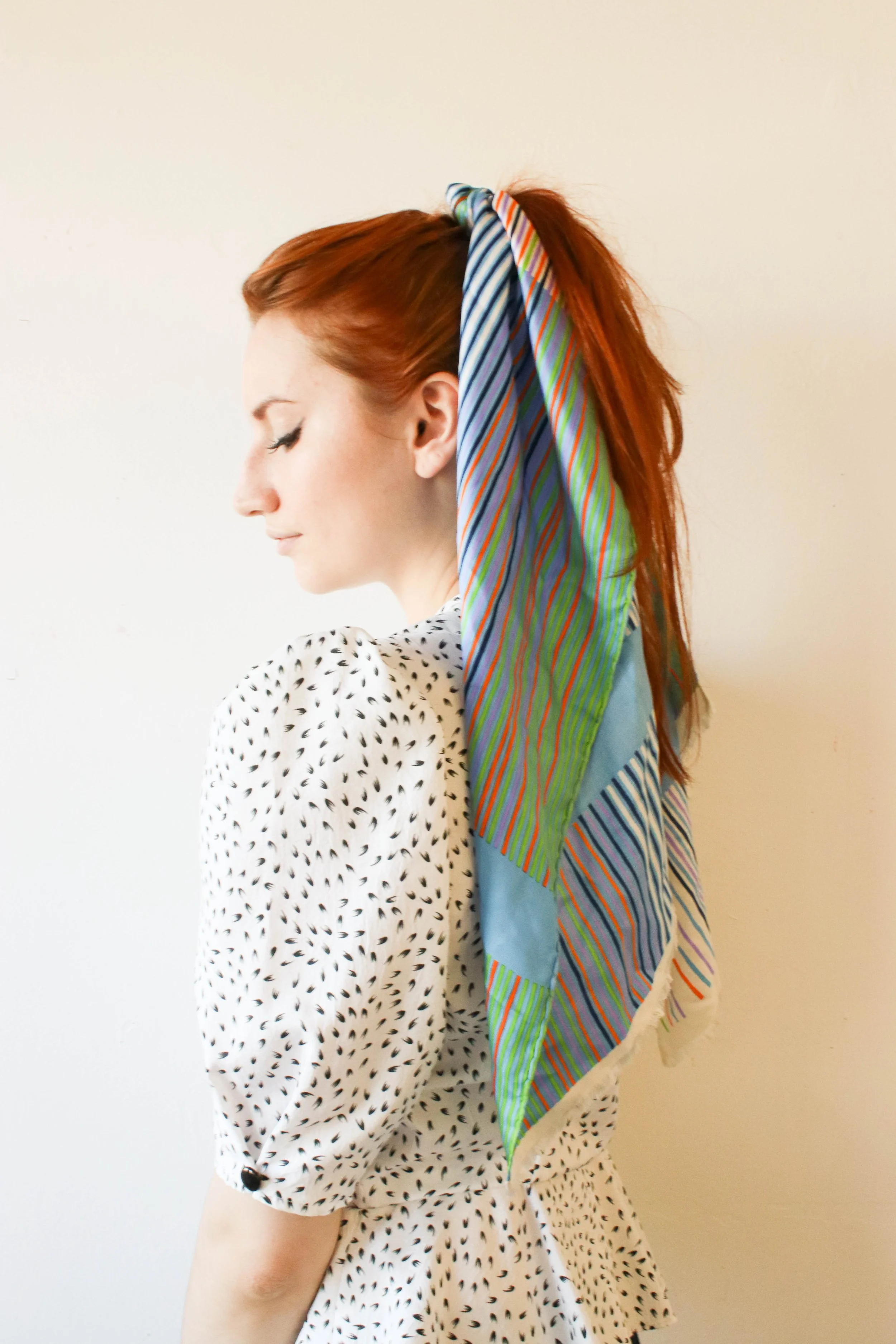 Side profile portrait of Louisa Rogers wearing a vintage puff sleeve blouse with a colourful striped headscarf tied into her red hair, styled in a soft and minimalist setting.