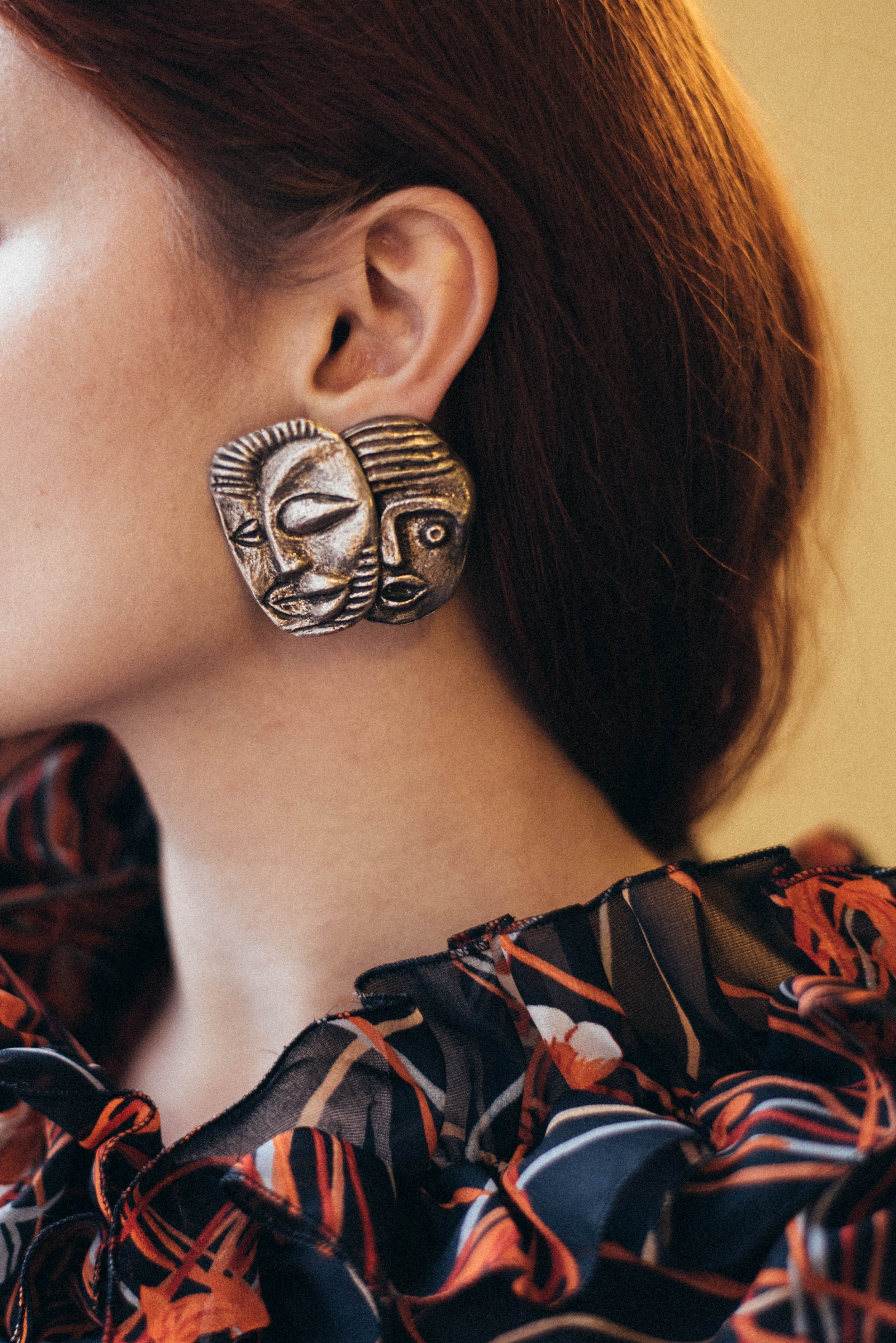 Close-up portrait of a woman wearing a large African mask-inspired earring, photographed by Marion Botella