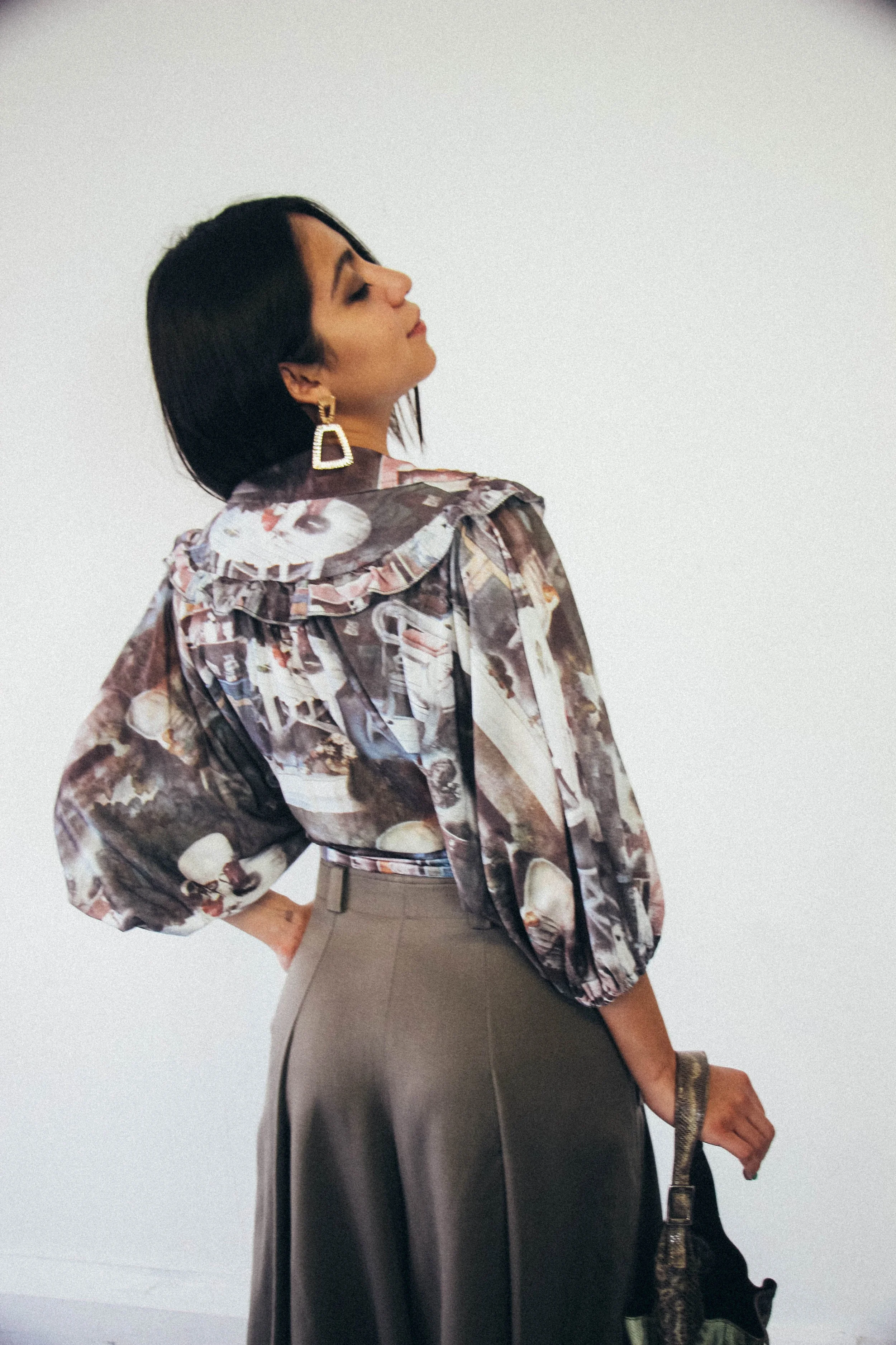 Annie wearing a printed vintage-style blouse with voluminous sleeves, structured olive trousers, and gold statement earrings, styled and photographed by Louisa Rogers with a soft editorial aesthetic.