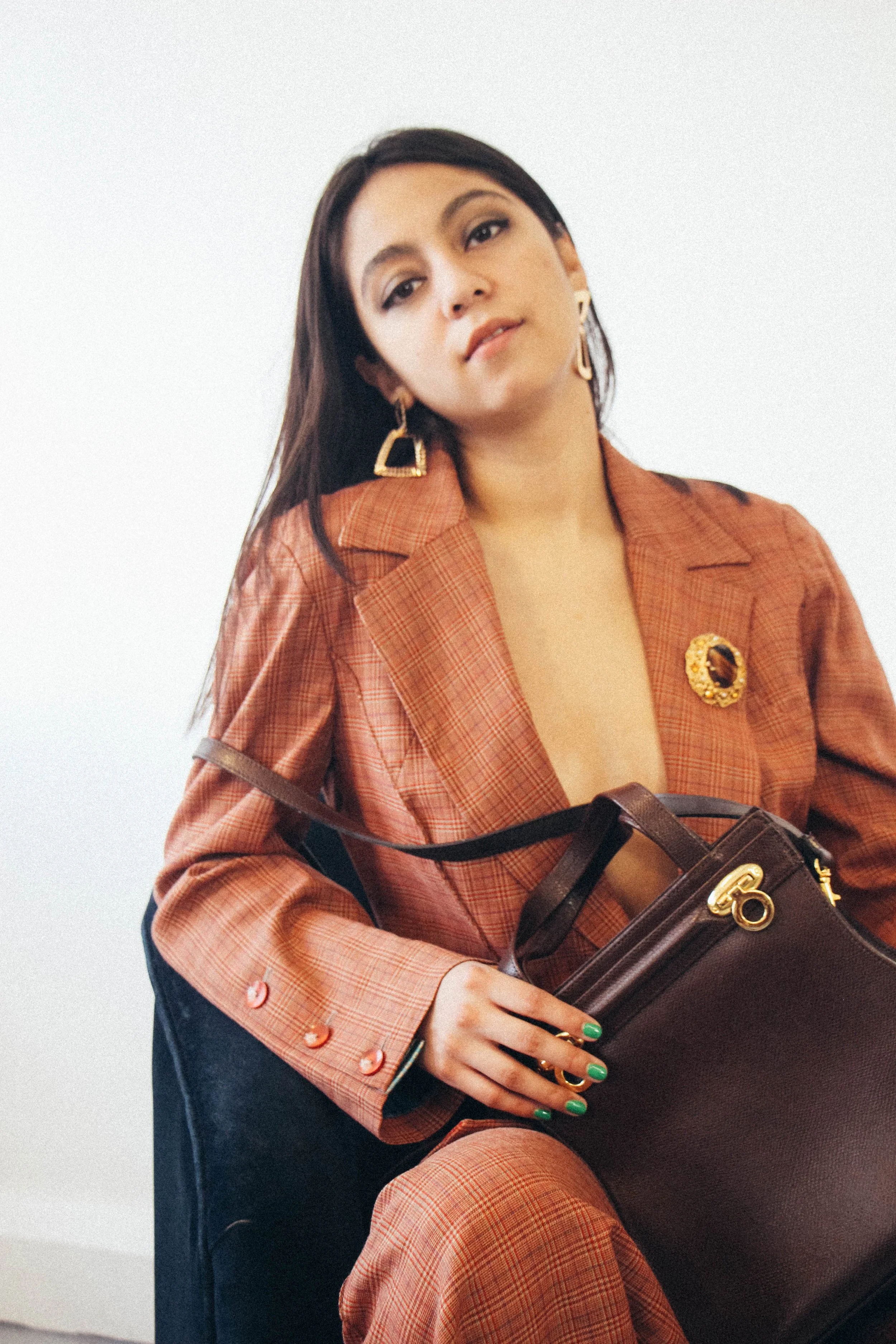 Annie wearing a rust-toned vintage check suit styled with gold statement earrings and a vintage Salvatore Ferragamo handbag, photographed by Louisa Rogers.