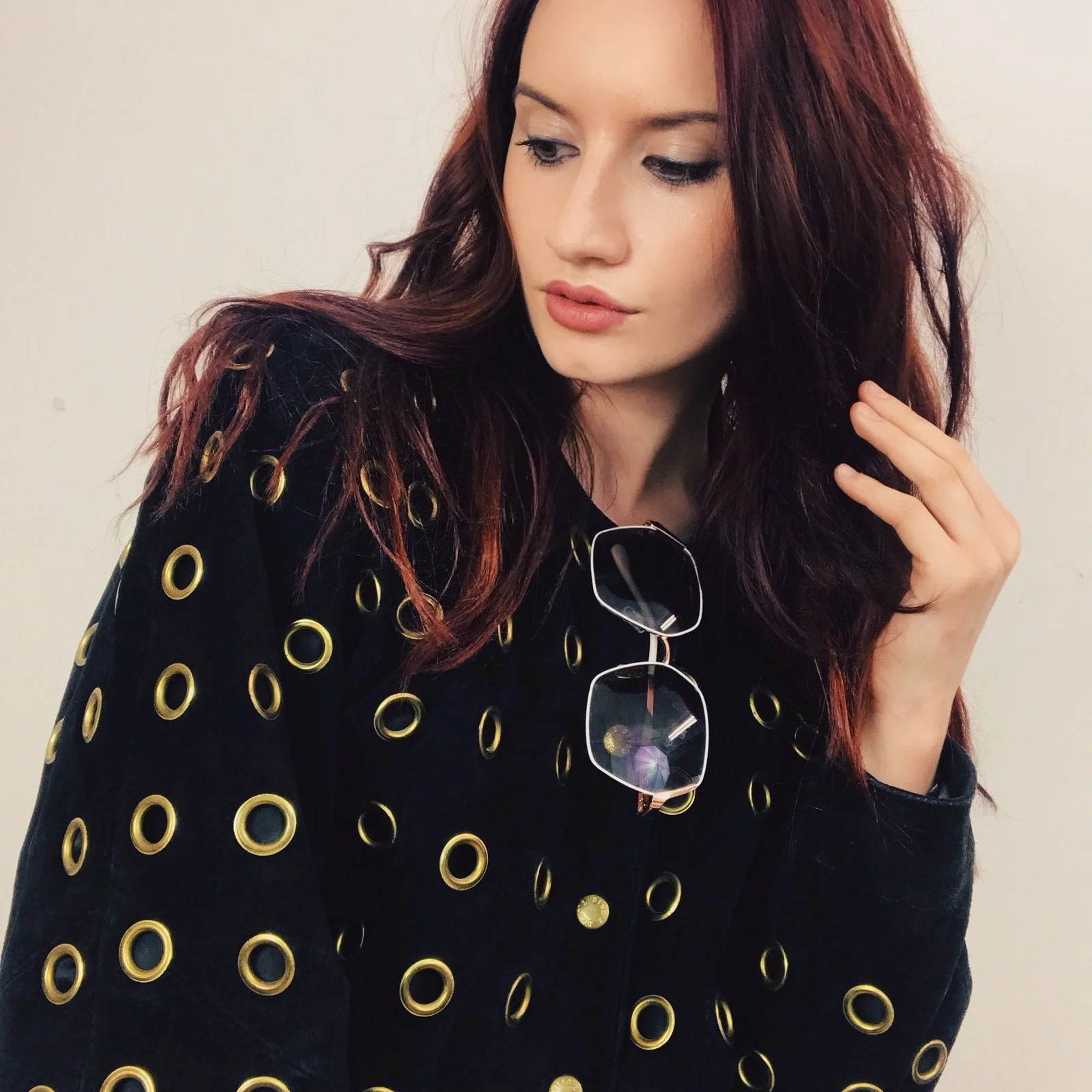 Portrait of Louisa Rogers wearing a vintage black jacket with gold eyelet detailing and retro sunglasses, styled and photographed in a minimalist studio setting.