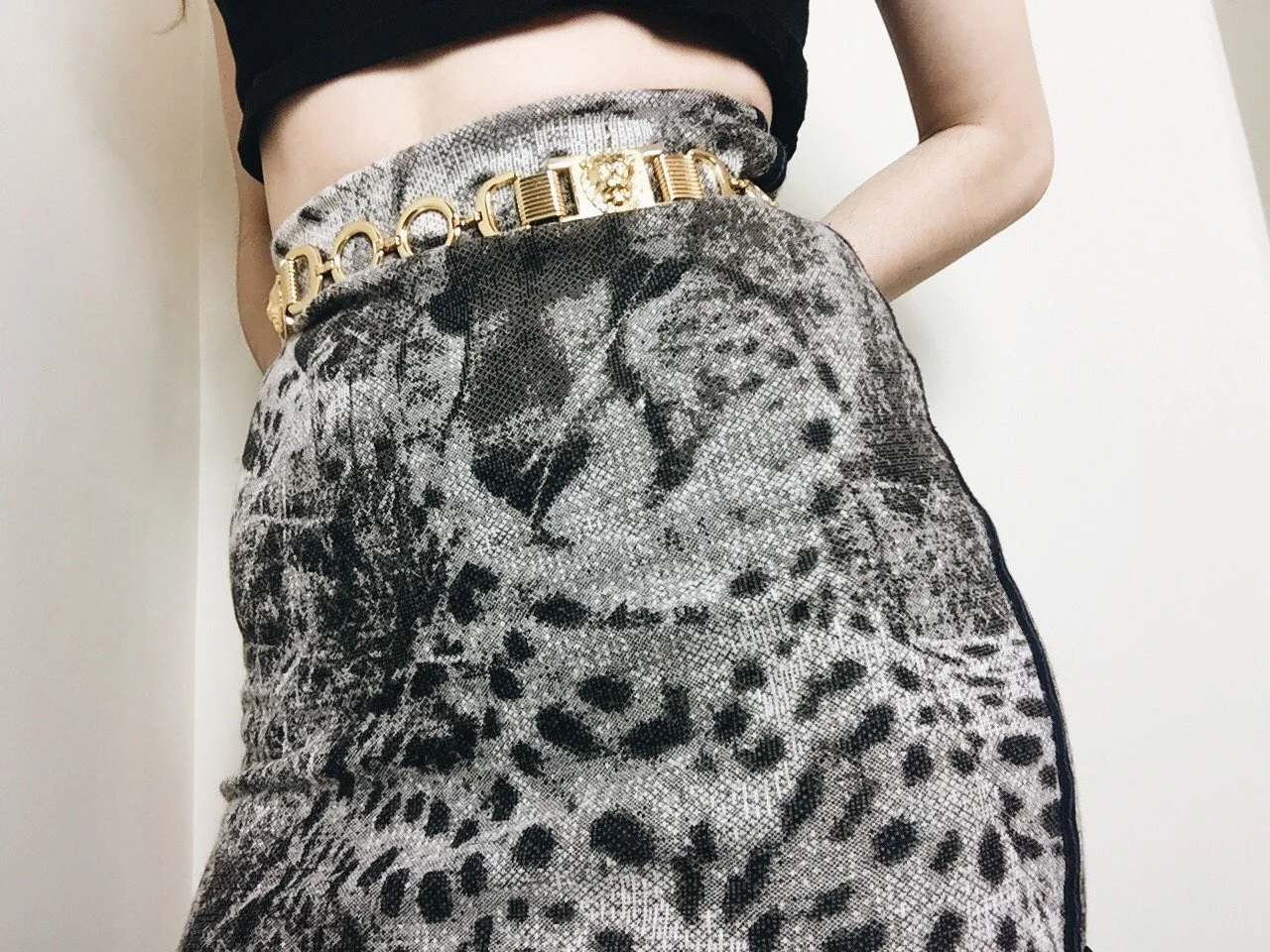 Close-up of a woman wearing a high-waisted jacquard skirt with a black and grey leopard print, accessorized with a vintage gold chain-link belt and black crop top.