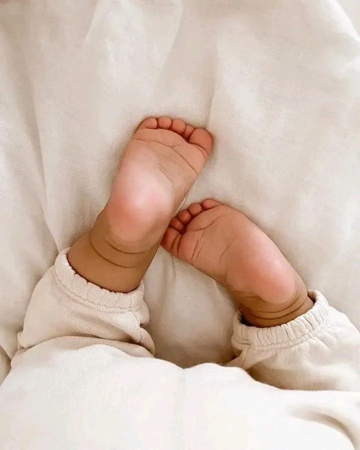 Close-up of a baby's feet and hands resting on a soft, cream-colored blanket or fabric.