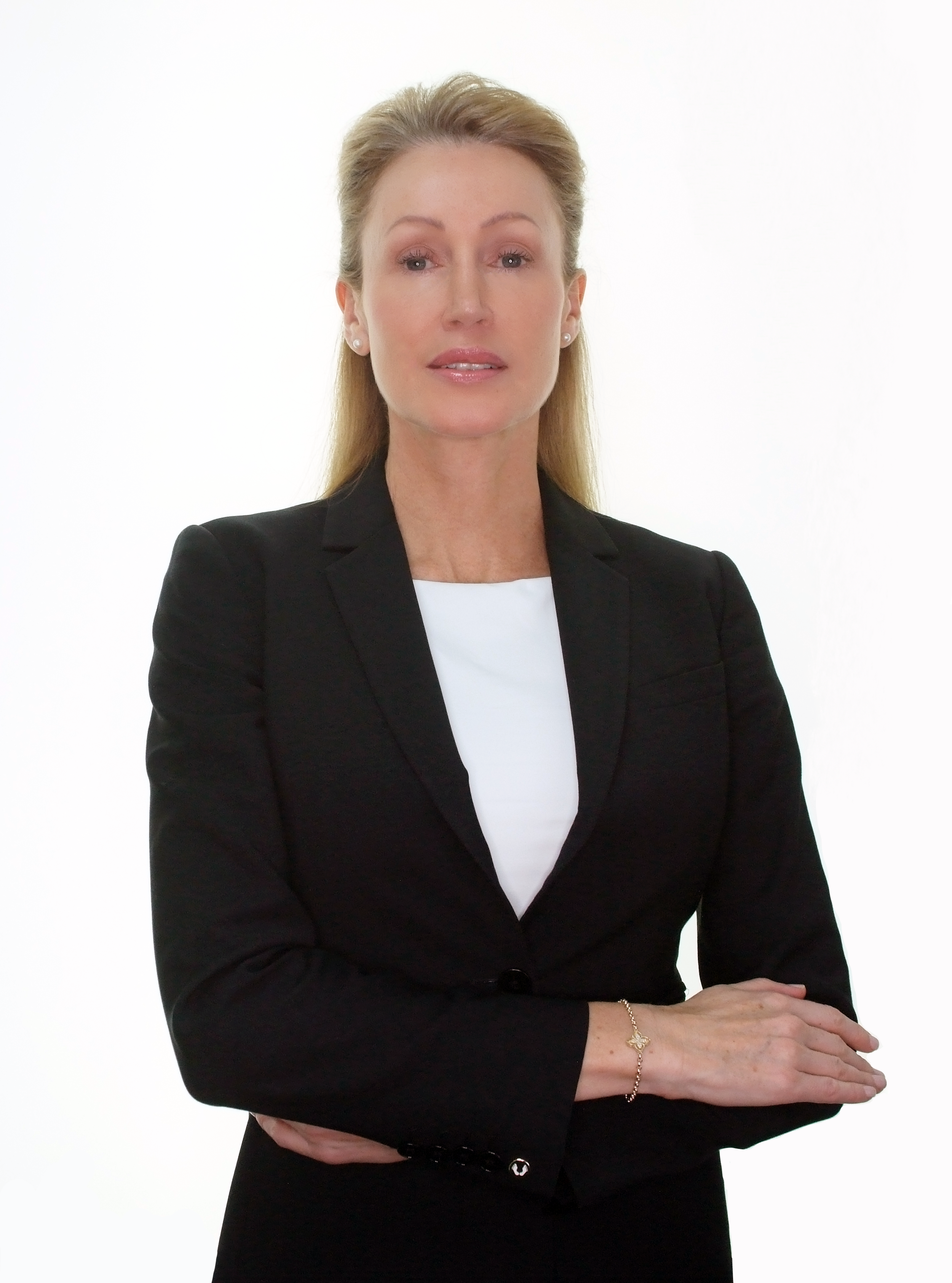 A woman with blonde hair, wearing a black blazer and white top, posing with her arms crossed against a white background.