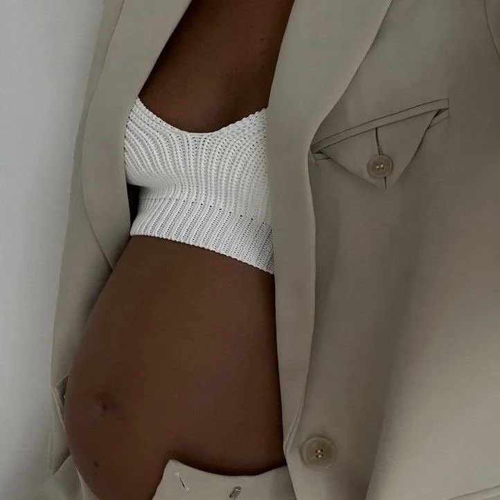Close-up of a woman's midsection showing her abdominal area, with a beige blazer and a white knitted top.