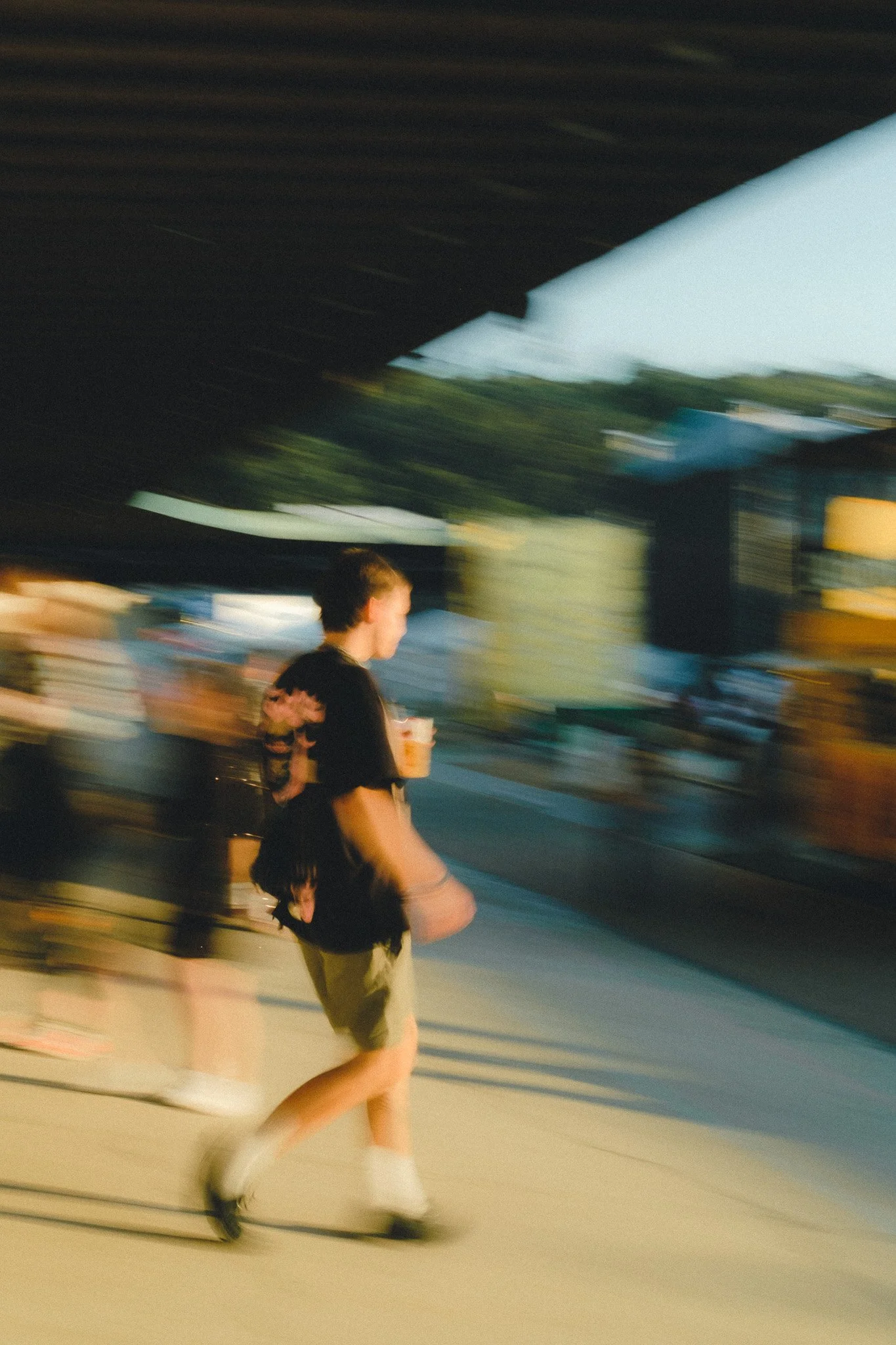 A person walking outdoors near a highway, carrying a drink, with blurred background indicating motion.