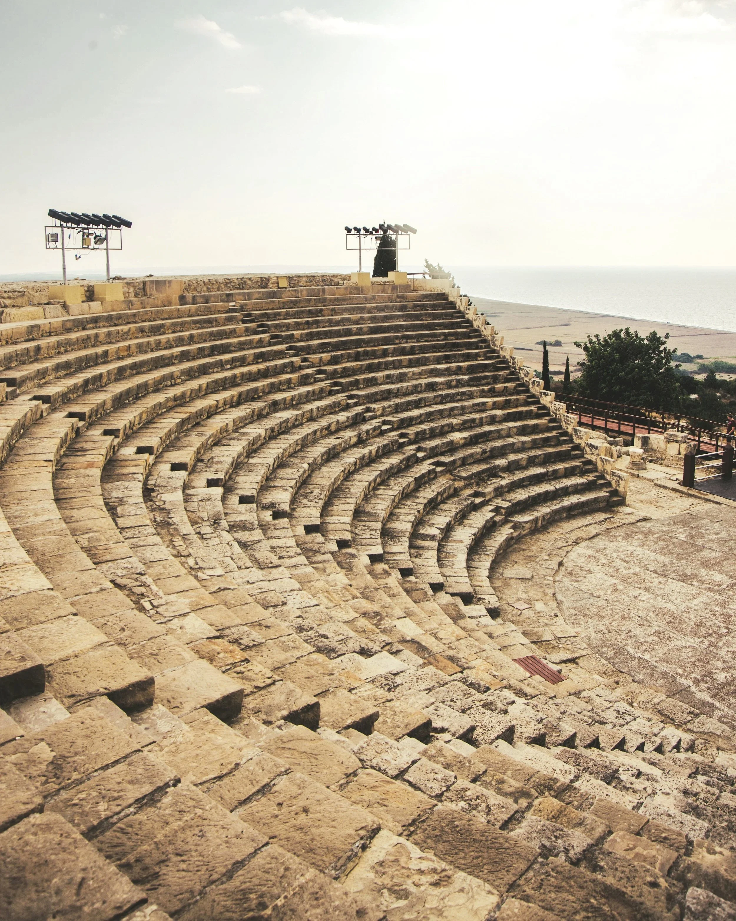 Ancient stone amphitheater with curved seating facing the sea, with stage area in front.