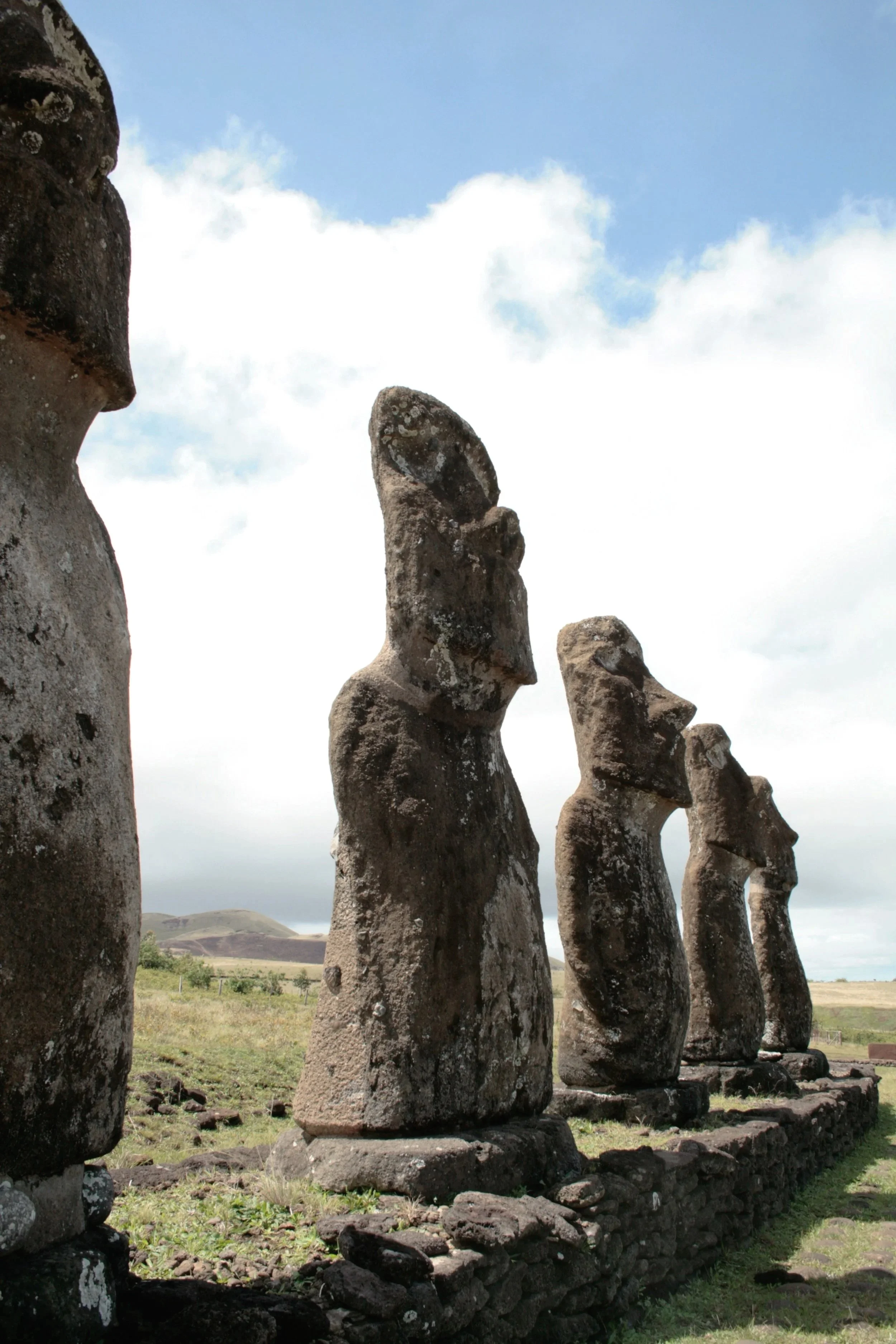 Five Moai statues on a stone platform in a grassy field, with a cloudy sky in the background.