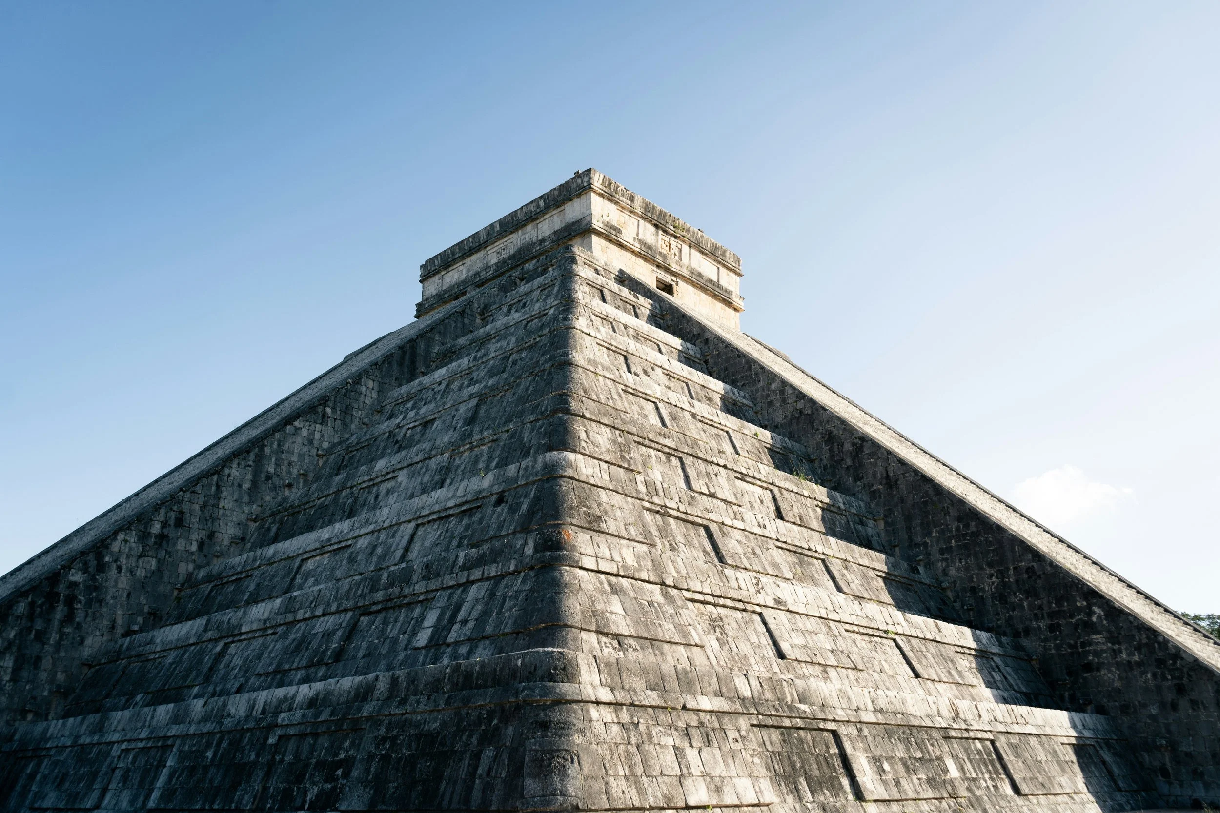 Low-angle view of ancient stone pyramid with a flat top against a clear blue sky.