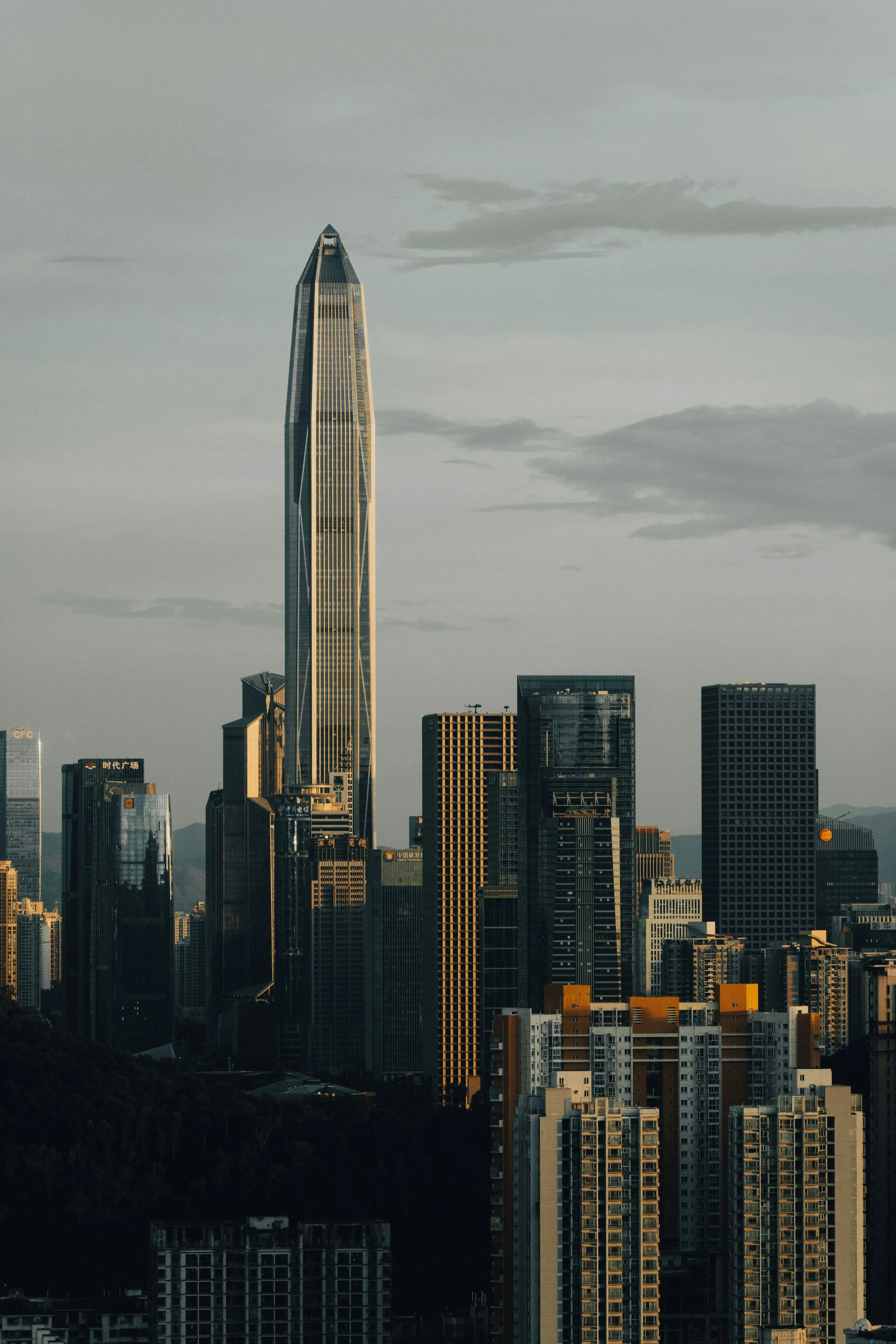 Skyscraper city skyline with a prominent tall, modern glass building in the center and other high-rise buildings surrounding it, under a cloudy sky.