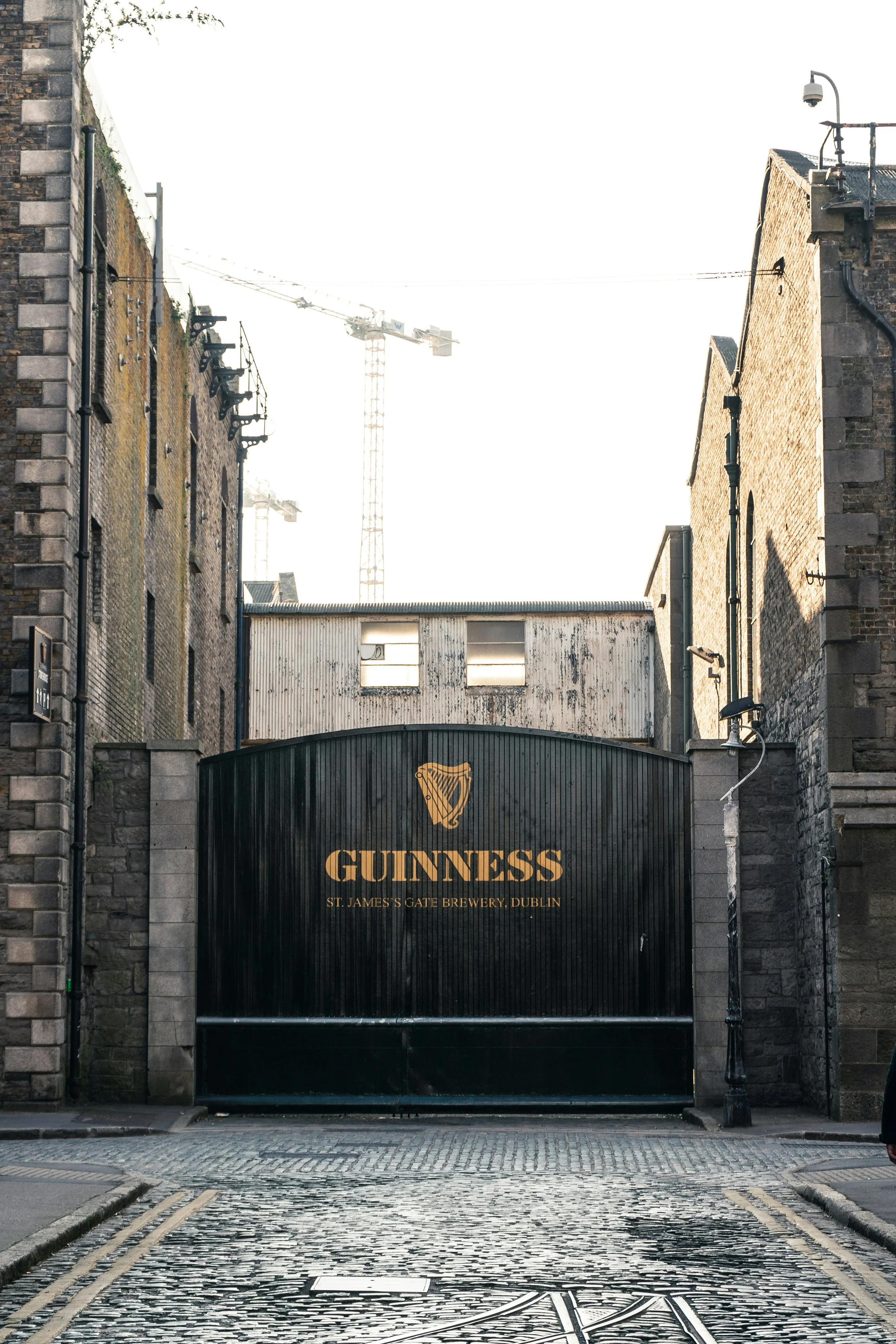 Black gate with Guinness logo and text for St. James's Gate Brewery in Dublin, surrounded by brick walls.