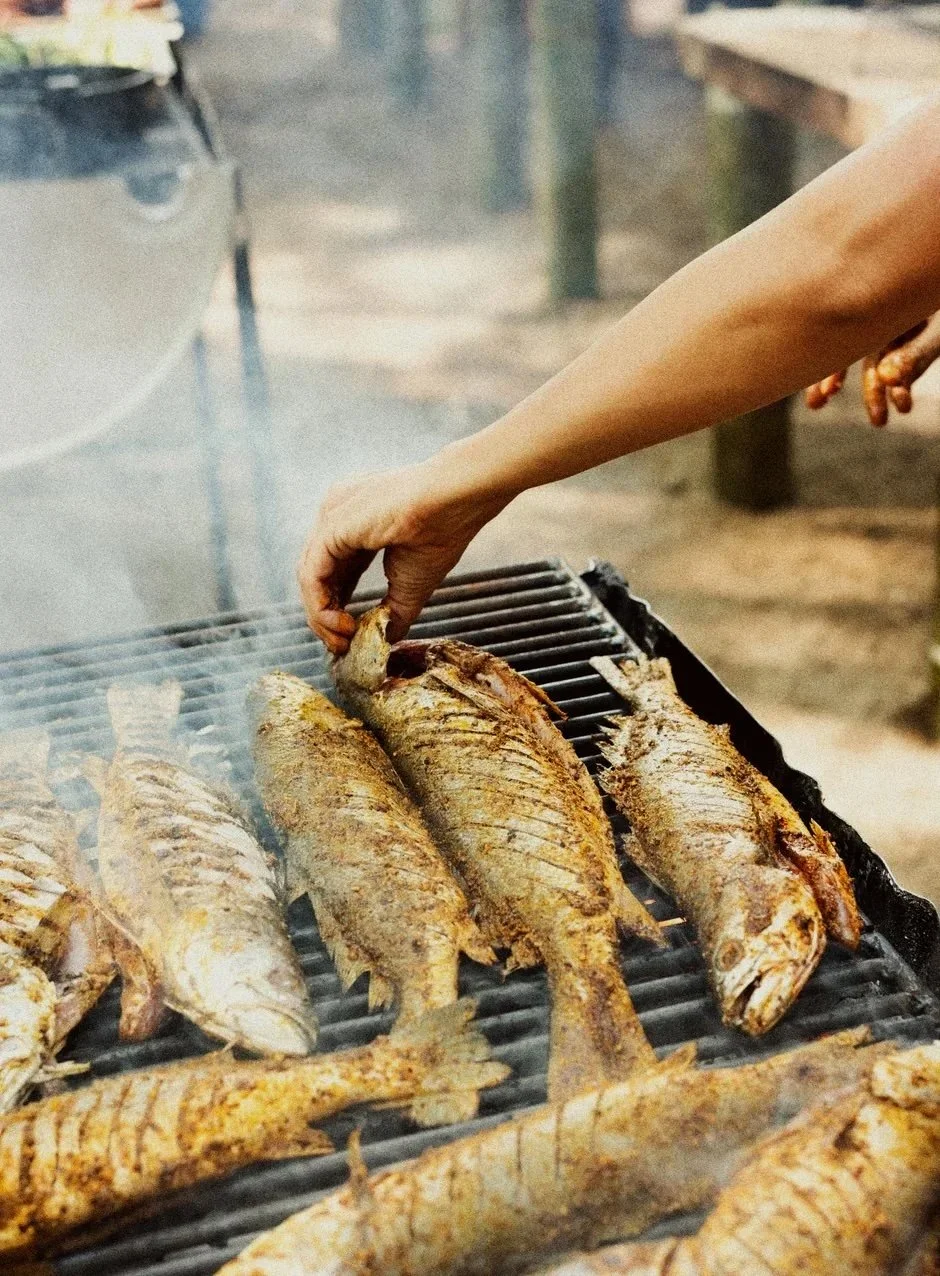 Person grilling several seasoned whole fish on an outdoor barbecue grill.