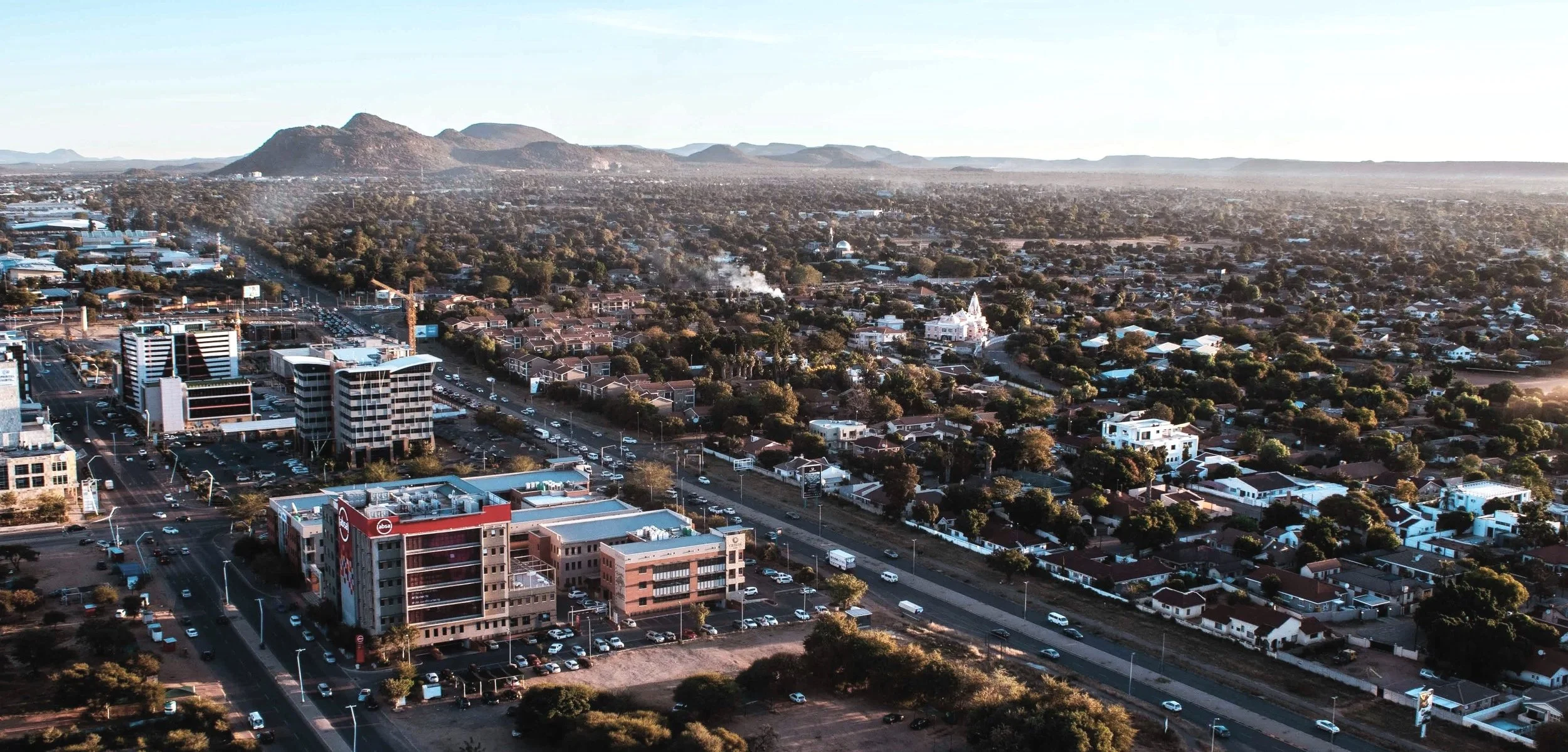 Aerial view of a city with a mix of tall buildings, residential houses, and a church, with mountains in the background during sunset.