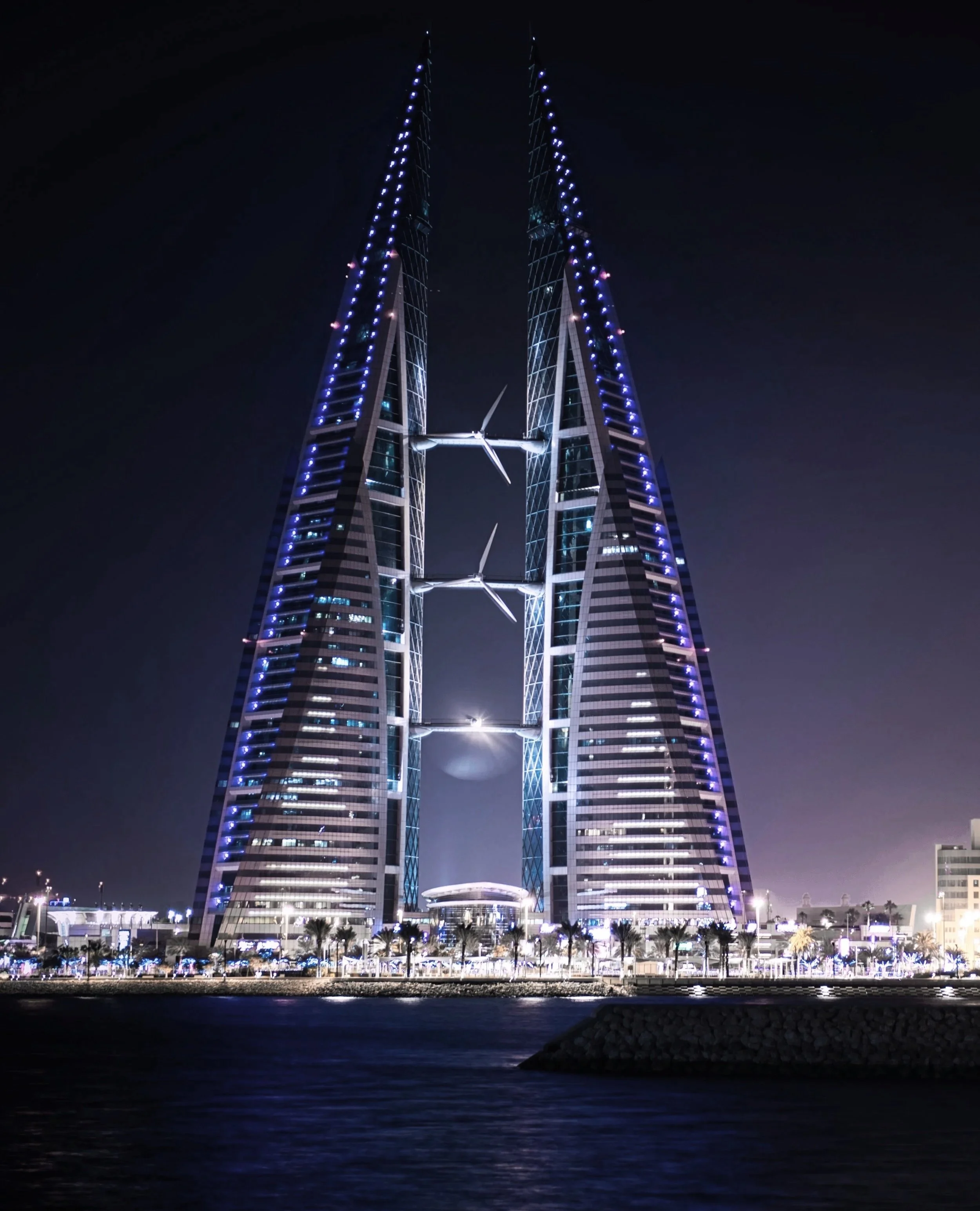 Night view of the illuminated Bahrain World Trade Center with two sail-shaped towers connected by three wind turbines.