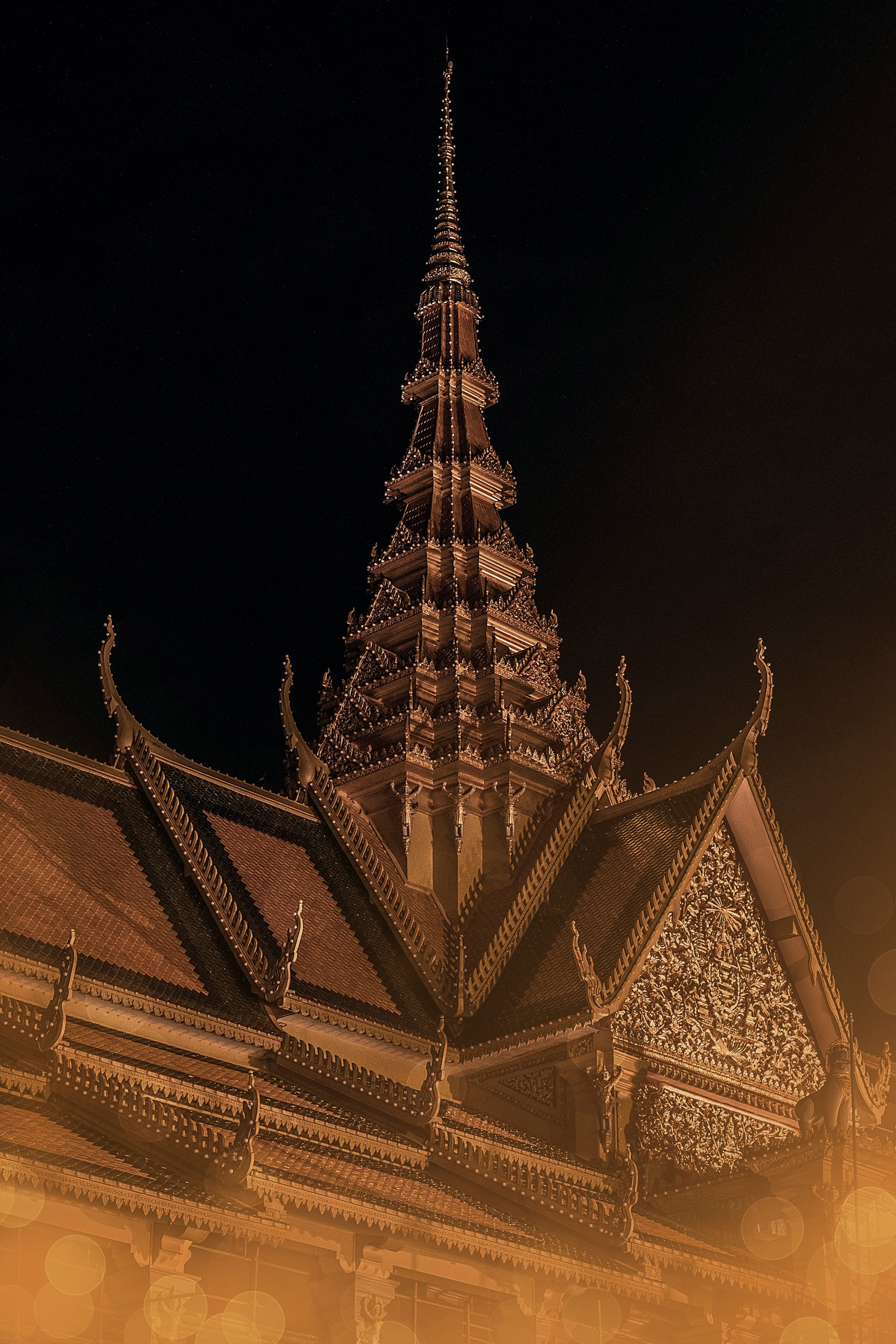 Night view of a traditional Thai temple with ornate architecture and tiered roofs, illuminated against the dark sky.