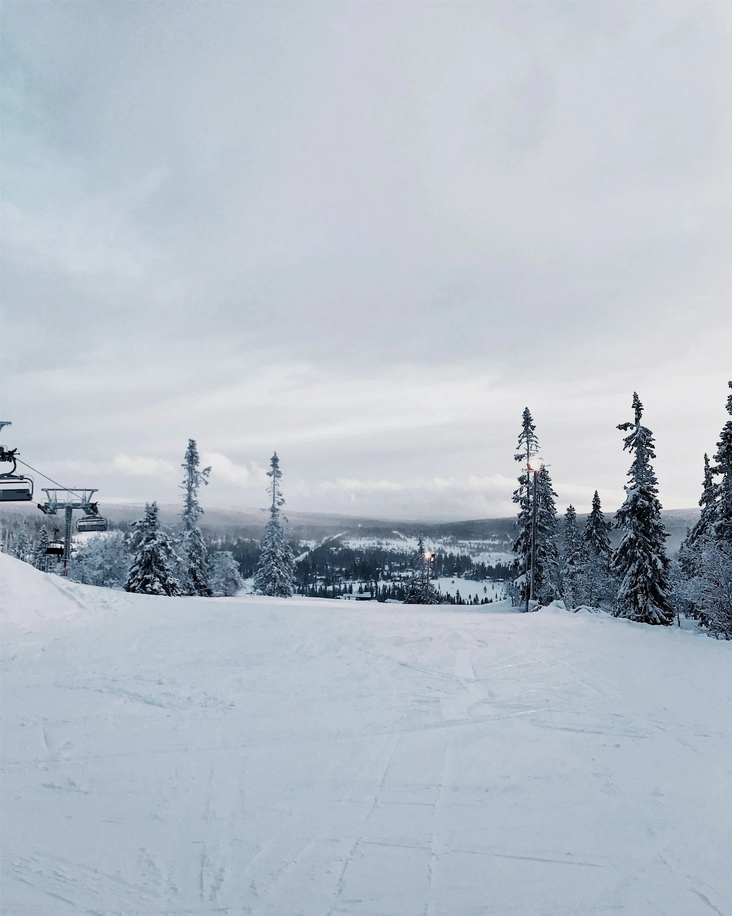 Snow-covered ski slope with trees, ski lift on the left, and overcast sky