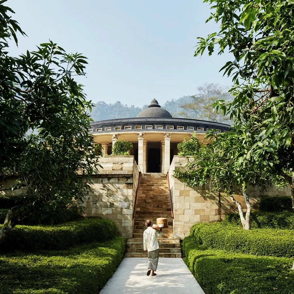 A person walking up stairs toward a circular pavilion with a domed roof, surrounded by greenery and trees.