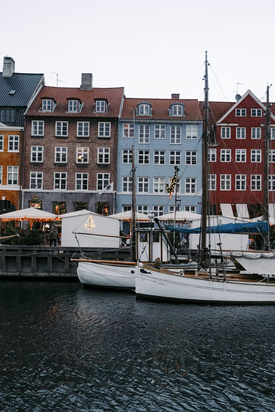 Colorful waterfront buildings with boats docked in front, decorated with Christmas lights and ornaments.