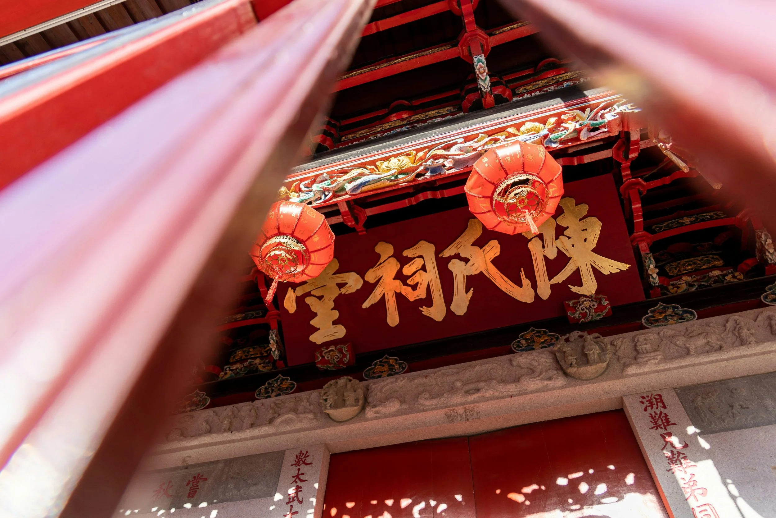 Close-up of a traditional Chinese temple entrance with red lanterns, ornate decorations, and gold Chinese characters on a red signboard.