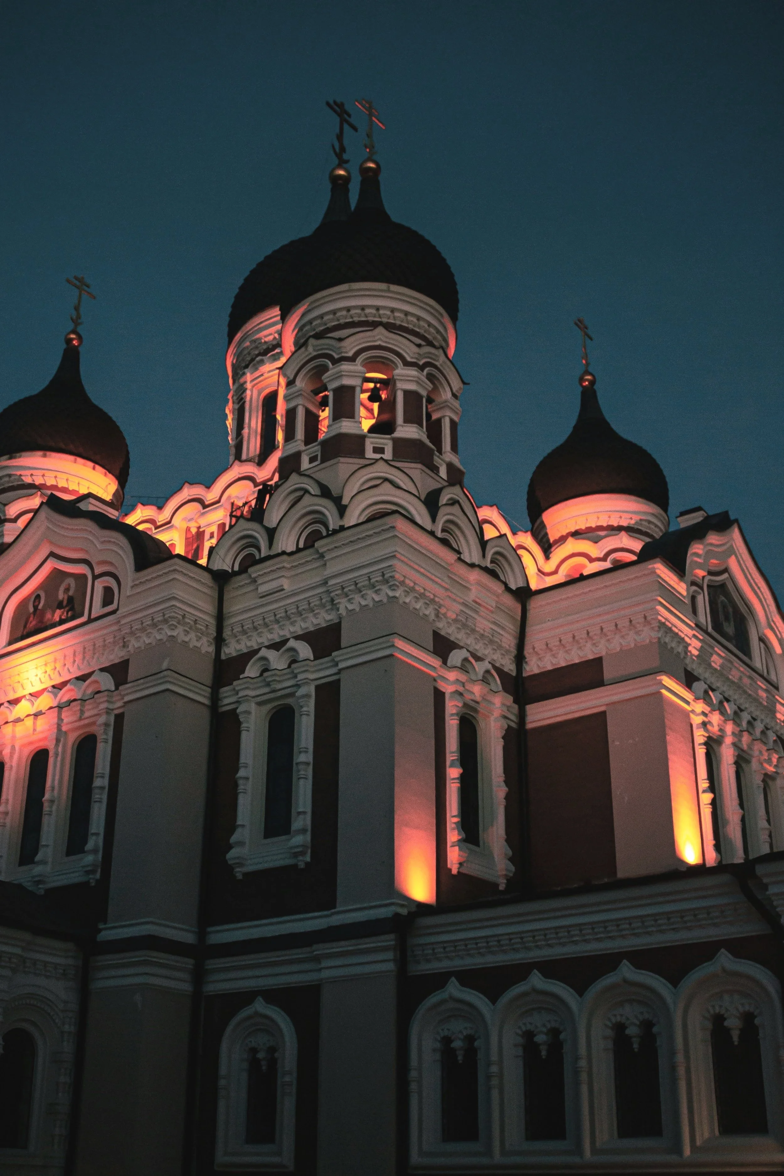 An illuminated Eastern Orthodox church with black domes topped with crosses, lit against a dark evening sky.