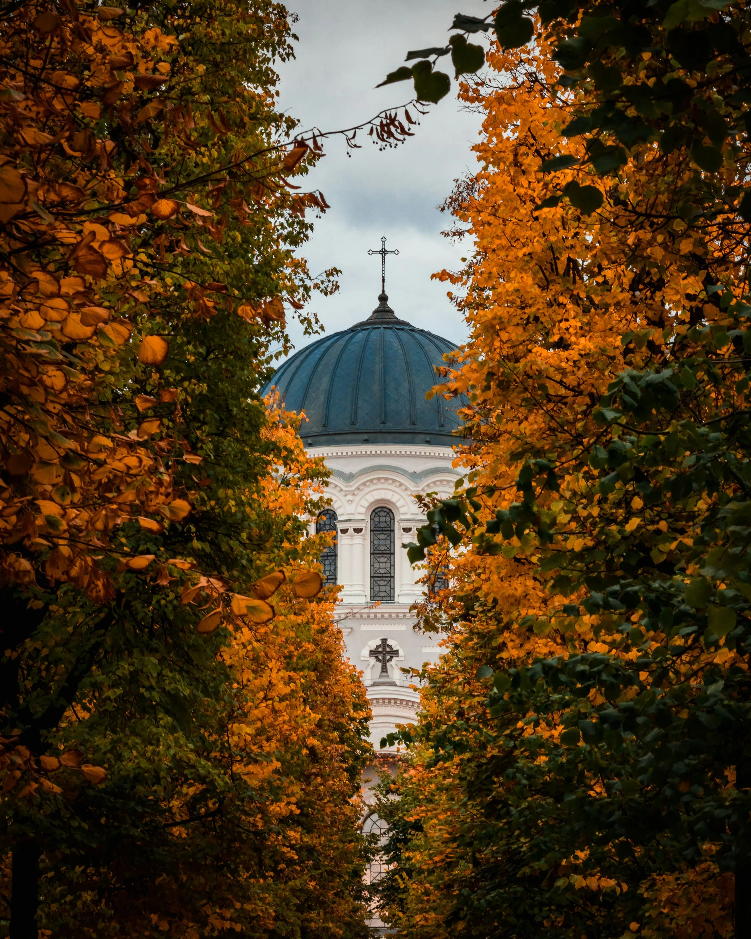A church with a blue dome and cross, framed by orange and green autumn trees.