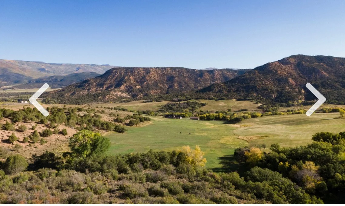 A scenic view of a valley with a golf course, surrounded by trees and hills under a clear blue sky.