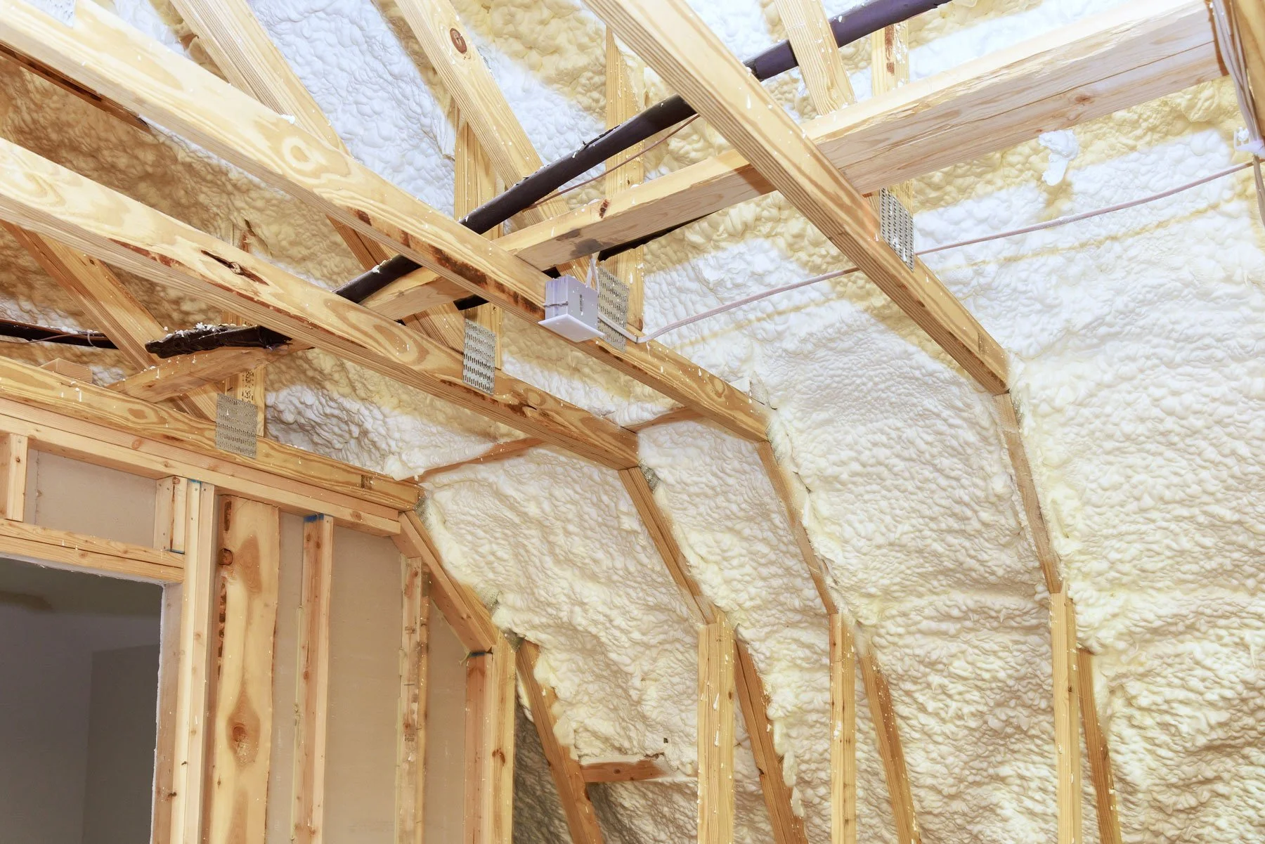 Interior of a building under construction with exposed wooden framing and spray foam insulation on the ceiling.