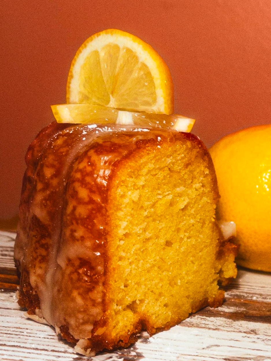 A lemon loaf cake topped with glaze and lemon slices, placed on a wooden surface with a whole lemon in the background.