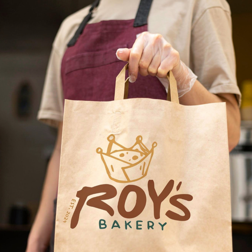 Person holding a paper bag with the logo 'Roy's Bakery' and a crown illustration.