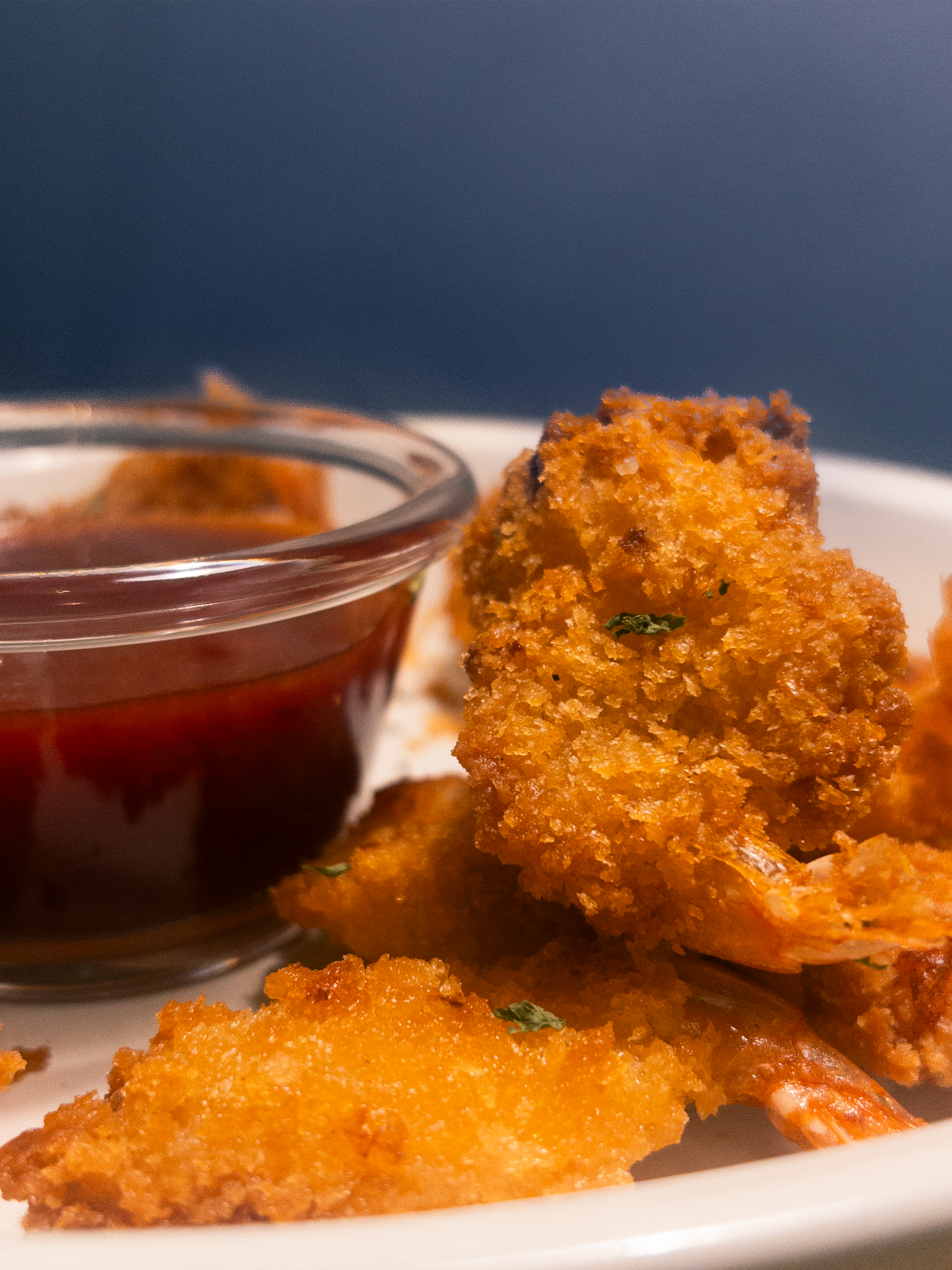 Close-up of crispy-fried shrimp with golden breading served with a small bowl of cocktail sauce.
