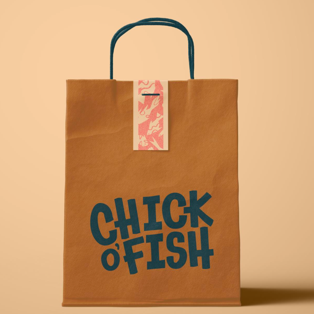 Brown paper bag with navy blue text that reads "CHICK O' FISH". The bag has two navy blue handles and a pink and white decorative tag attached at the top.