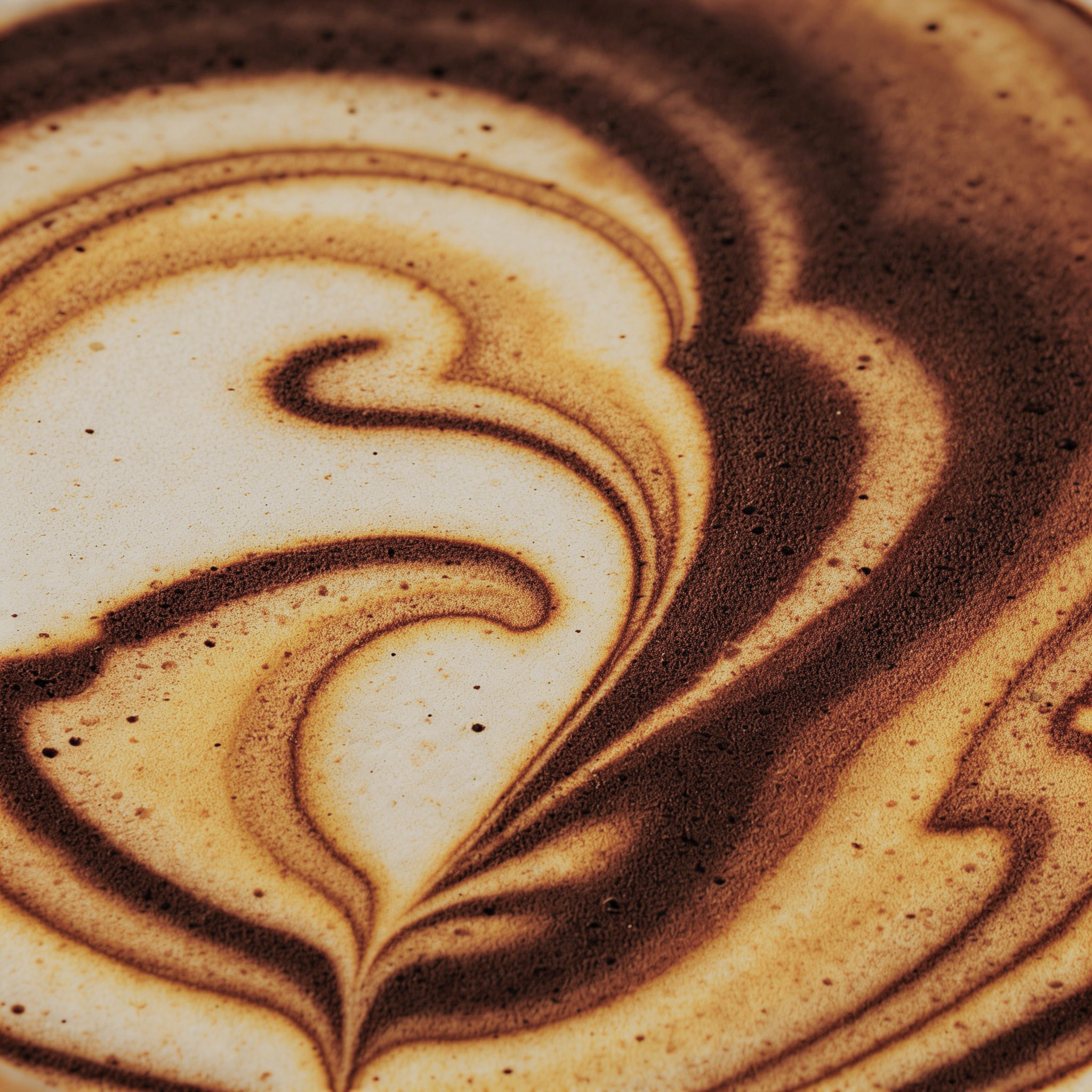 Close-up of a latte art design with brown and beige swirls in coffee.