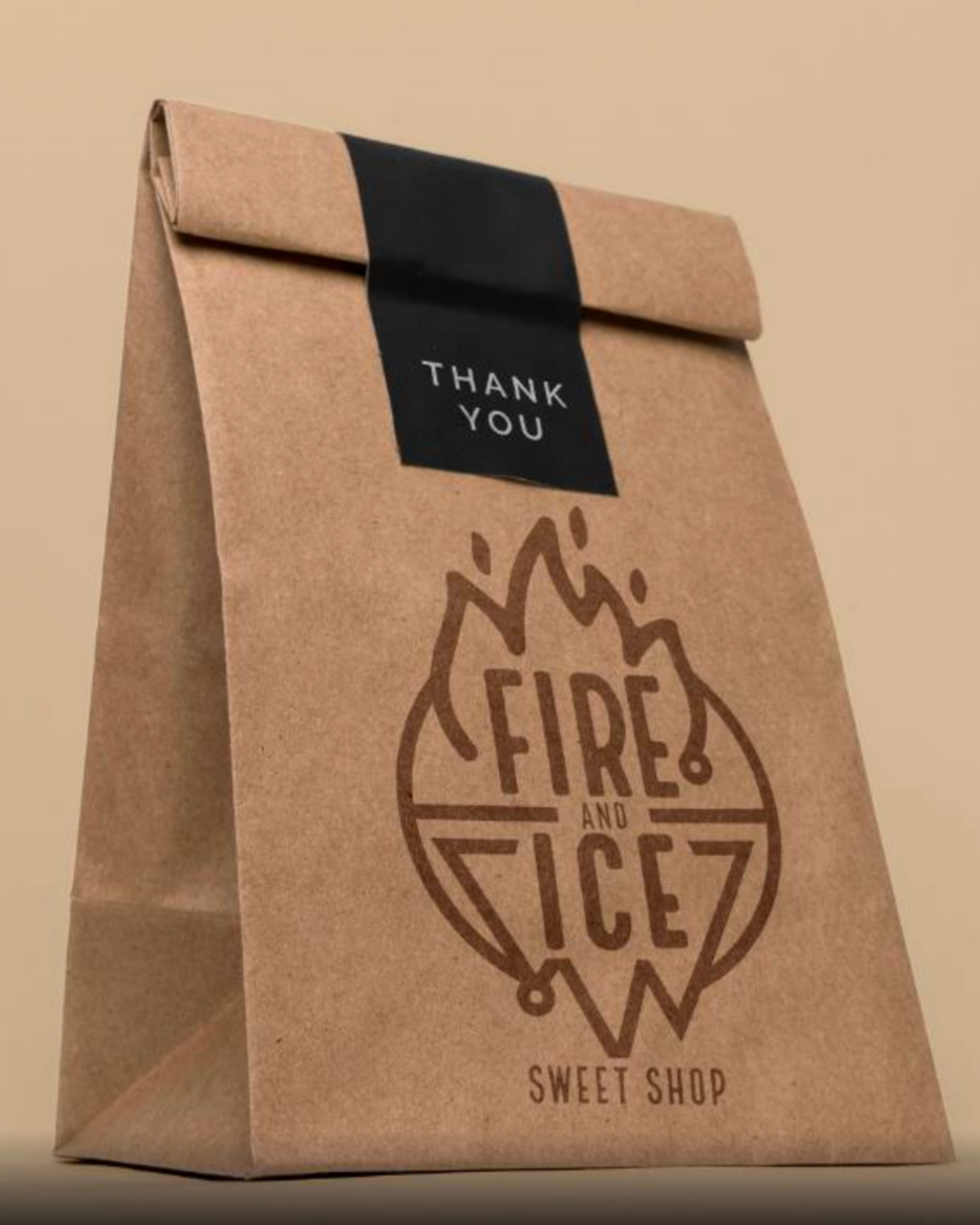 Brown paper bag with a black label that says 'Thank You'. The bag has a logo with a flame, crossed lines, and the words 'Fire and Ice' inside a circle, and 'Sweet Shop' at the bottom.
