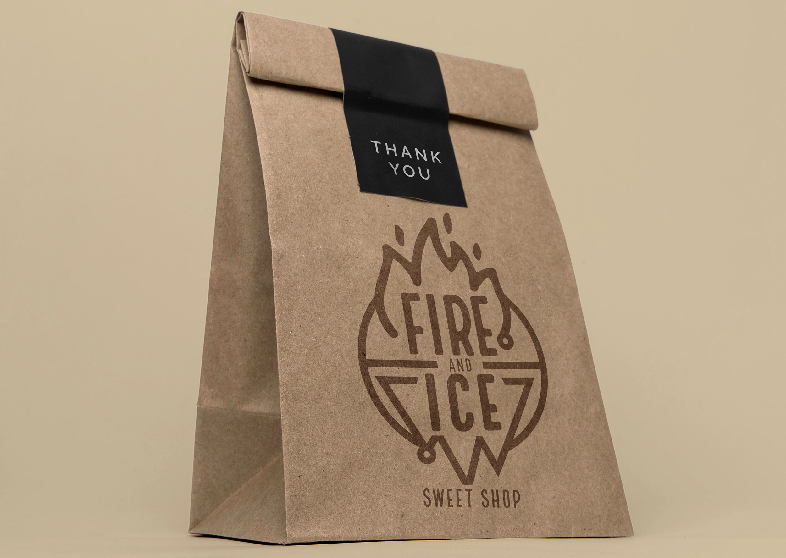 A brown paper bag with a black thank you sticker on top, displaying a logo of a mountain shape with walking figures, and the words 'Sweet Shop' below.
