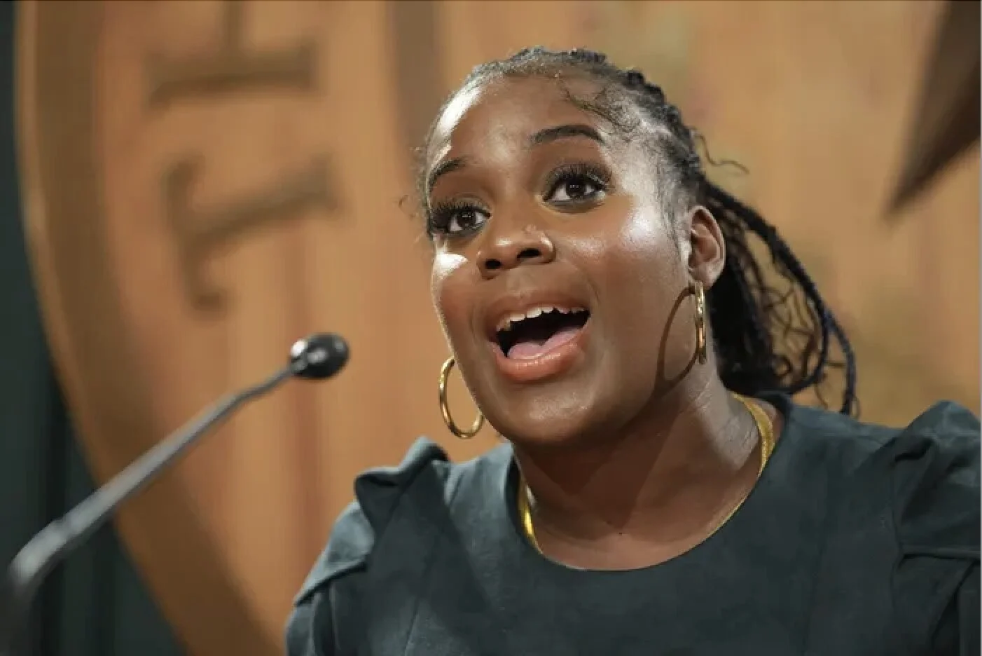 A young man in a checkered shirt concentrating on a computer screen in a computer lab with other people working at computers in the background.