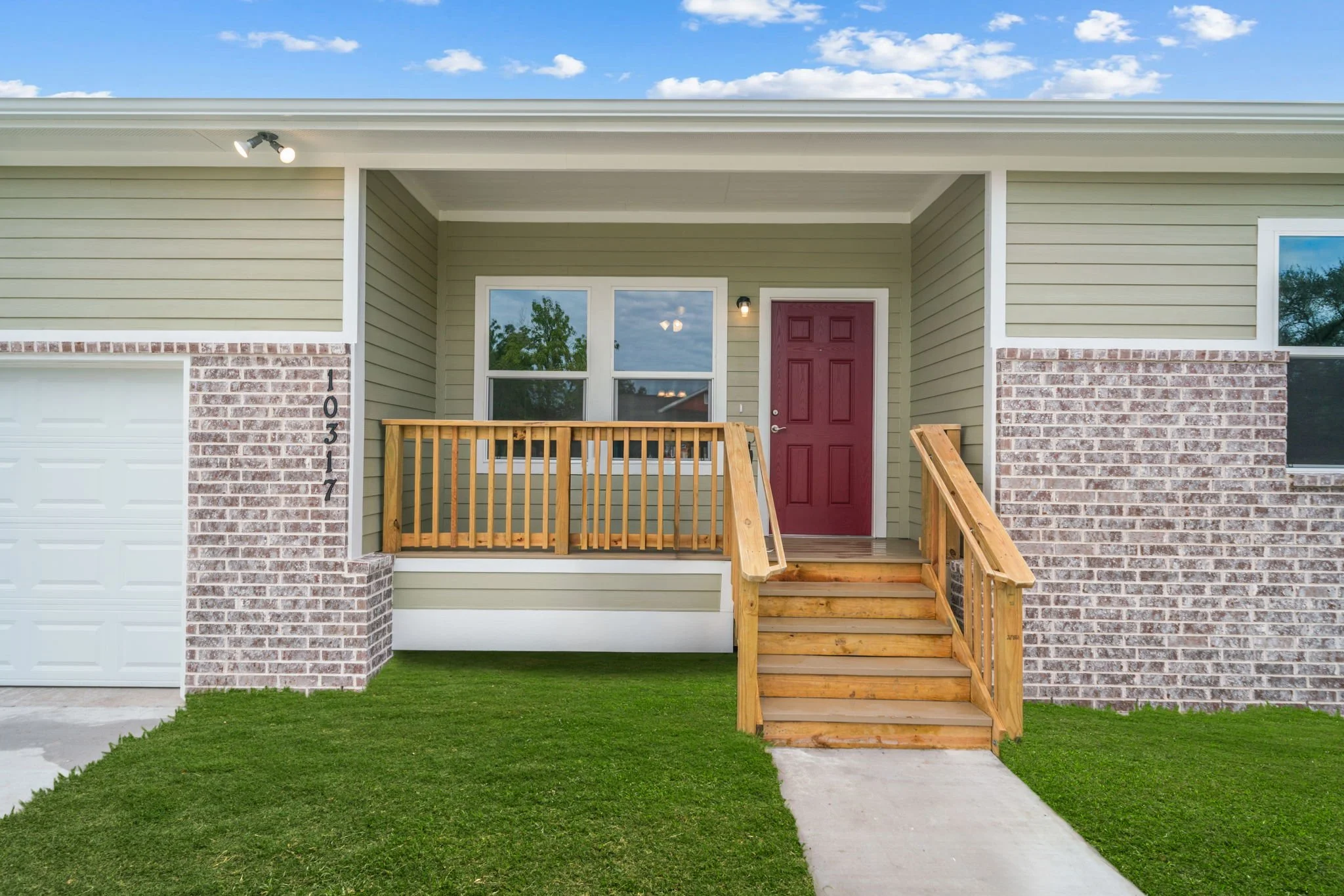 Front porch of a new house with a red door, green siding, brick accents, a small wooden staircase, and a lawn.