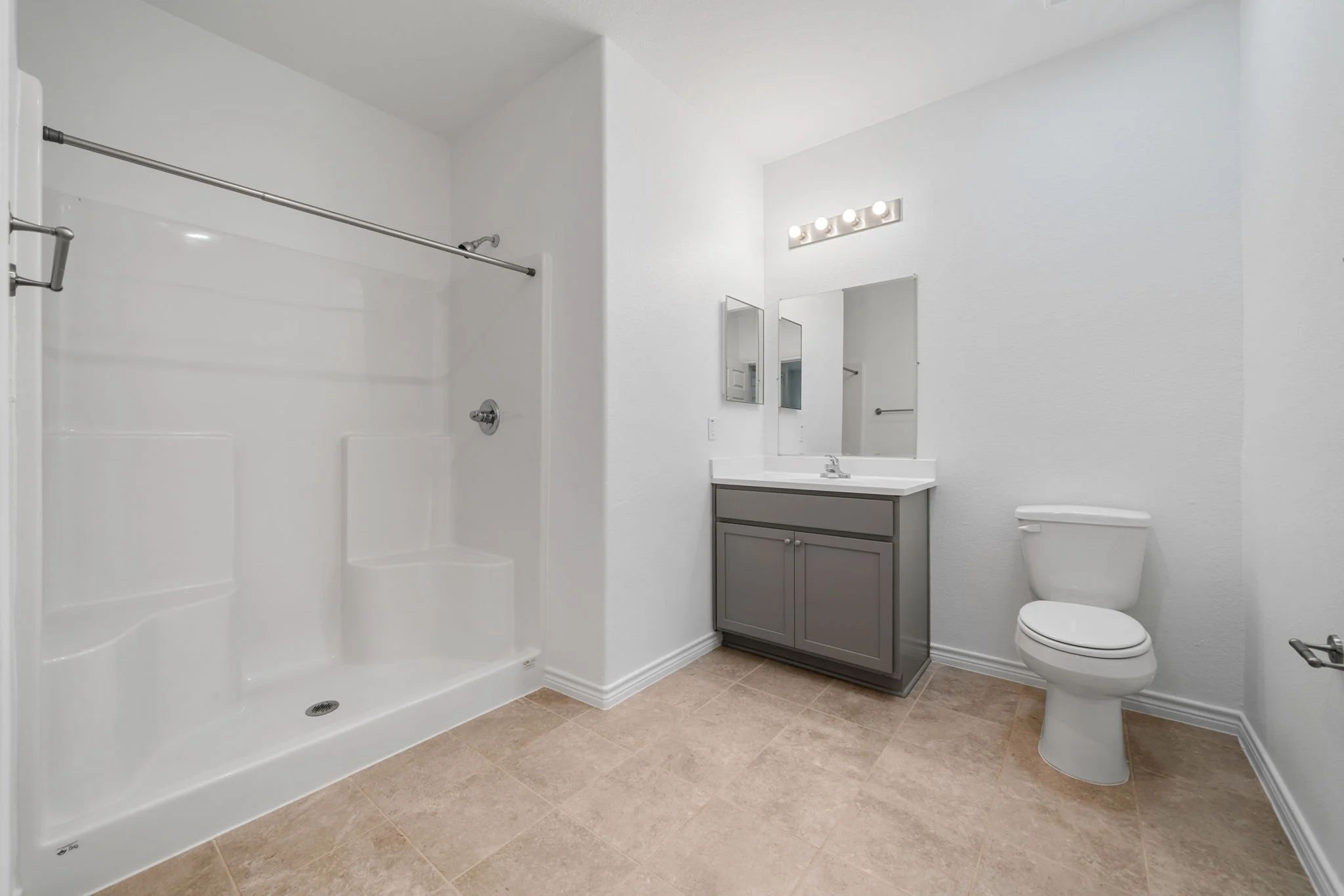 Bathroom with a white shower stall, gray vanity with a mirror, toilet, beige tile floor, and white walls.