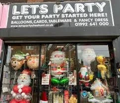 Storefront display with festive Christmas decorations and plush Santa Claus toys in window, advertising party supplies.